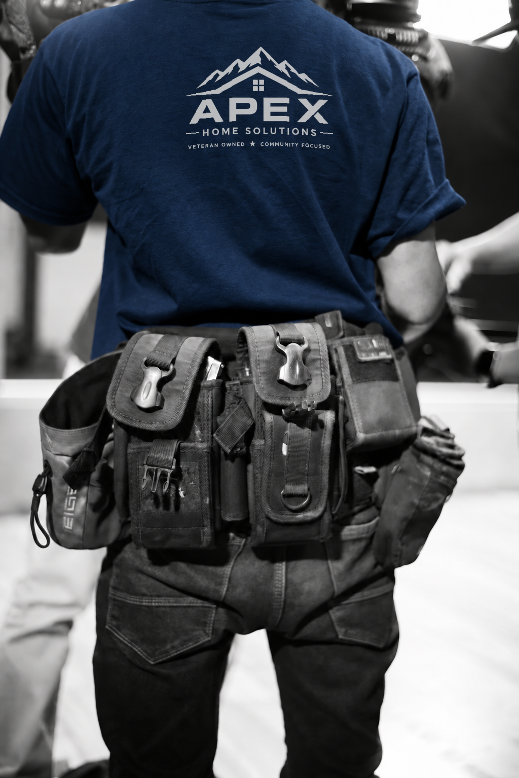 A person wearing a blue T-shirt with 'APEX Home Solutions' logo and a tool belt with various tools.