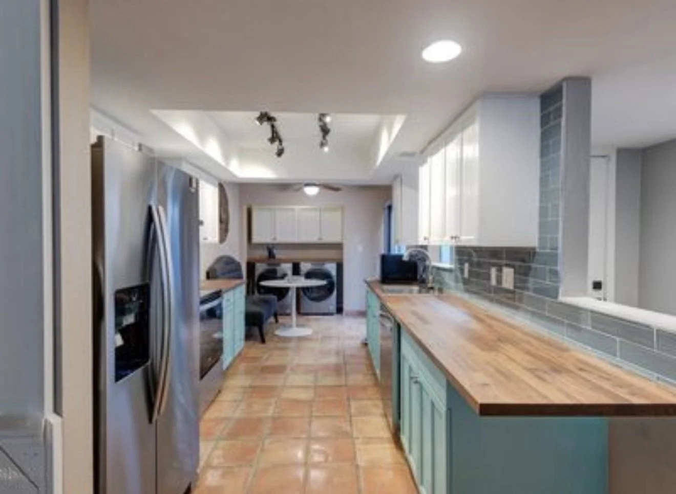 A spacious kitchen with mint green cabinets, a wooden countertop, stainless steel appliances, tiled backsplash, and a small breakfast nook.
