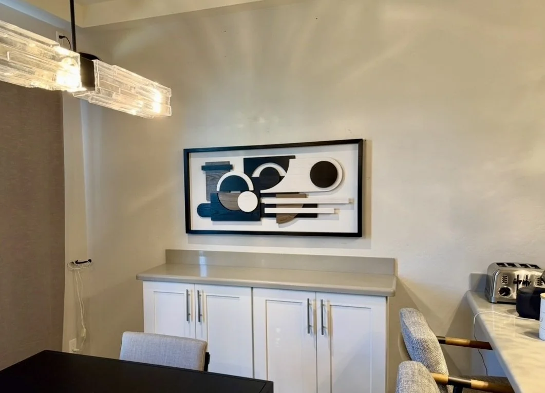 Modern dining room with abstract wall art, white cabinetry, and a marble countertop, featuring a hanging light fixture and kitchen appliances.