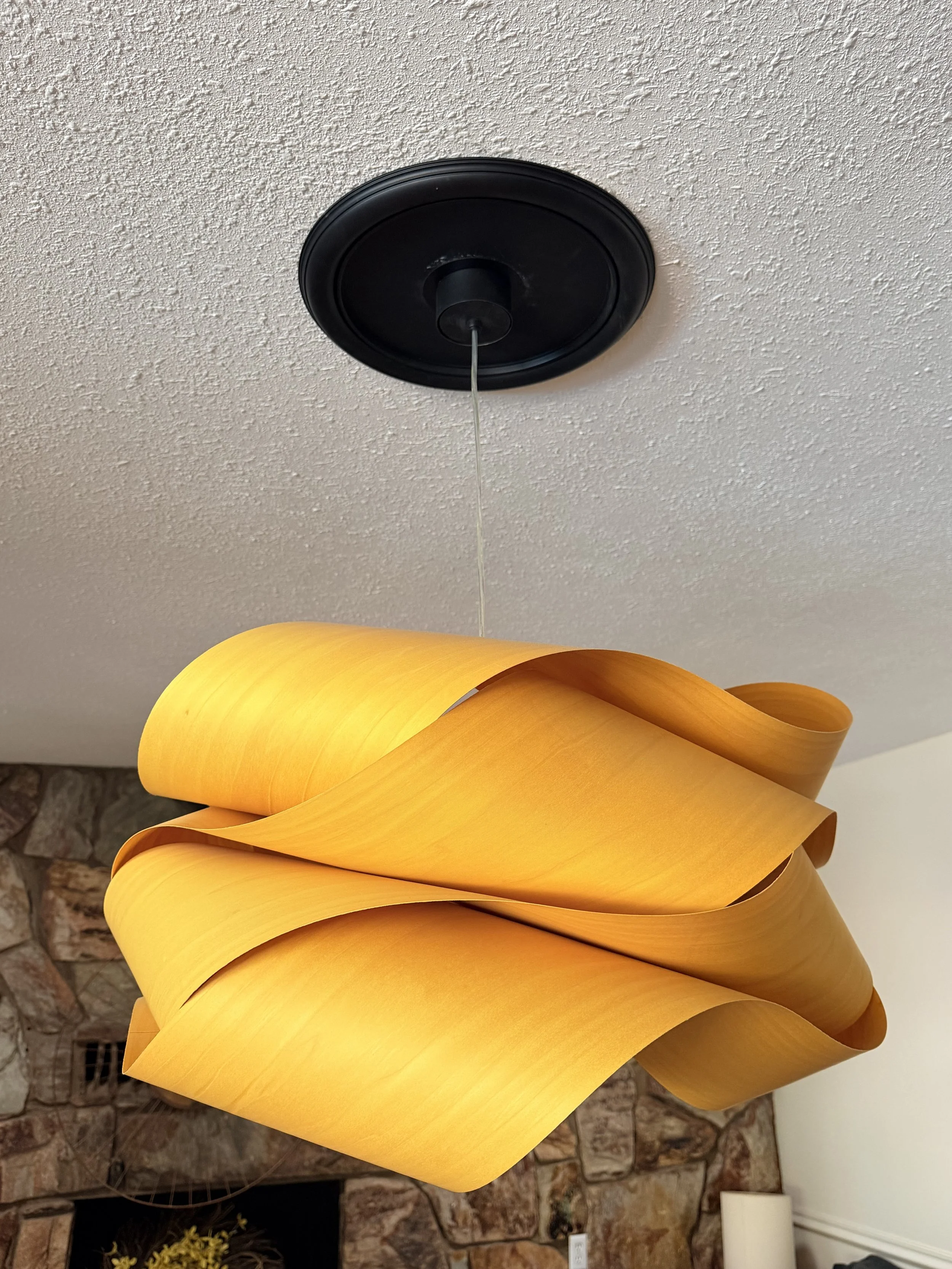 A yellow, modern, sculptural pendant light with multiple twisted, curved layers hanging from a black ceiling mount.