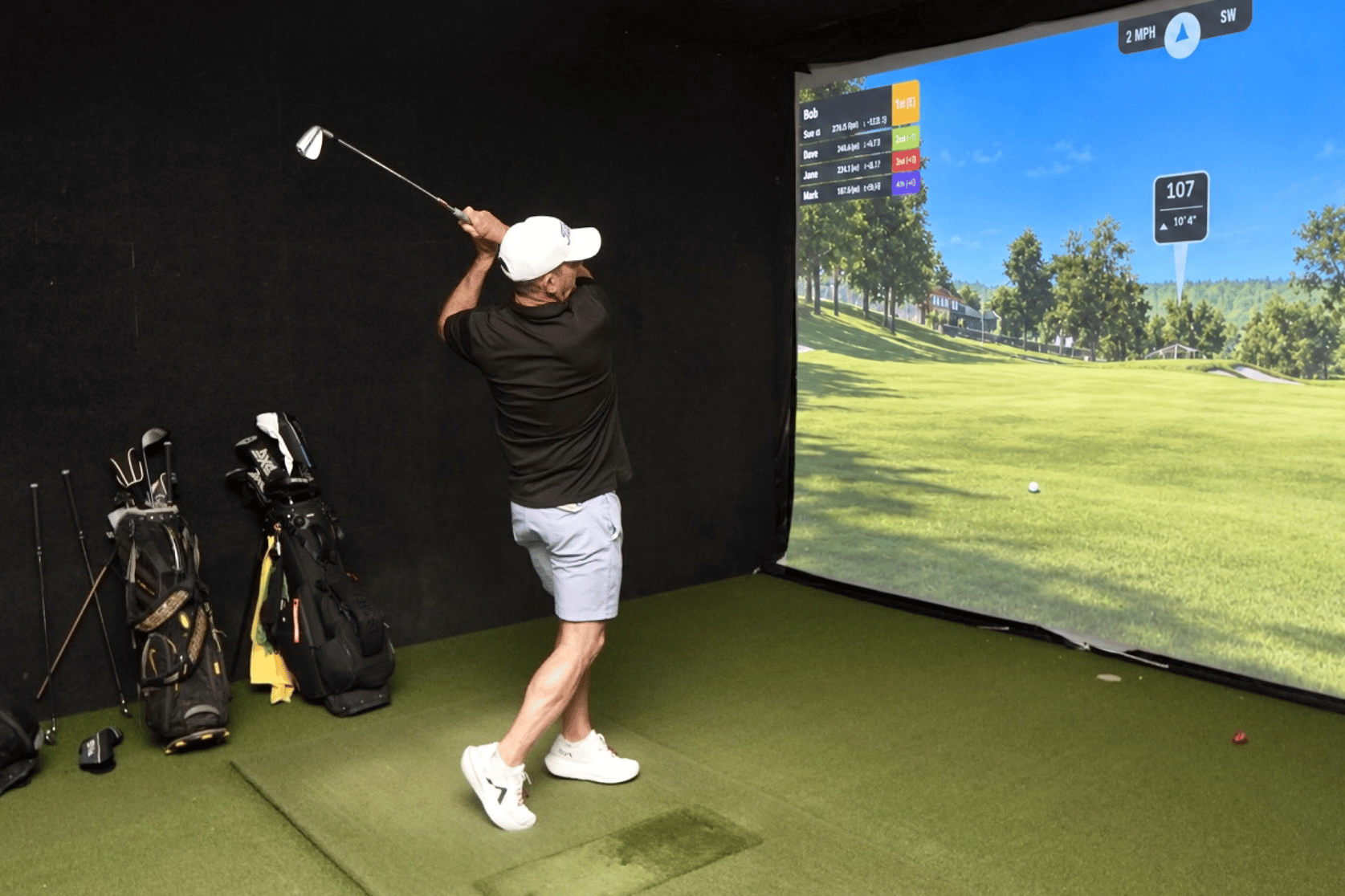 Golfer practicing indoors in a golf simulator, swinging a club toward a projected virtual course.