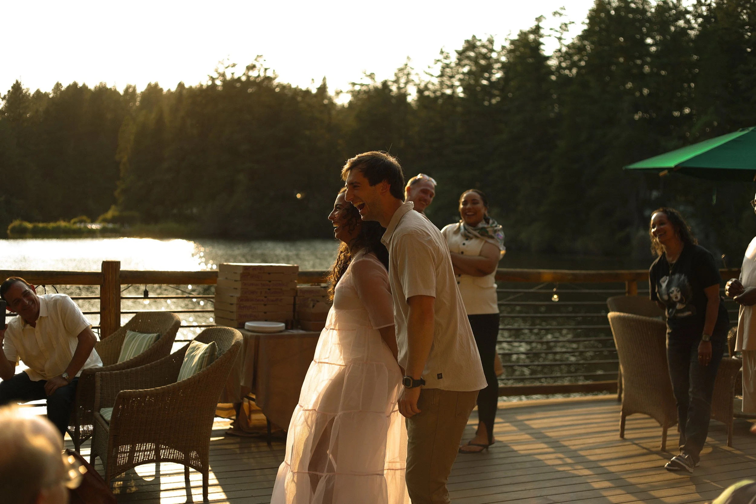 People enjoying an outdoor gathering by a lake during sunset, smiling and socializing.