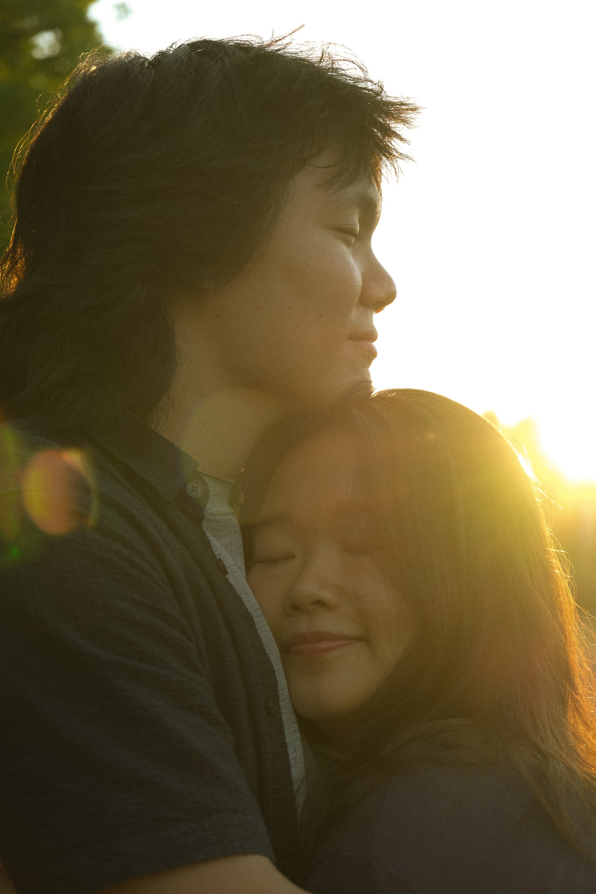 A close-up of a young man and woman with their eyes closed in an embrace, illuminated by warm sunlight.