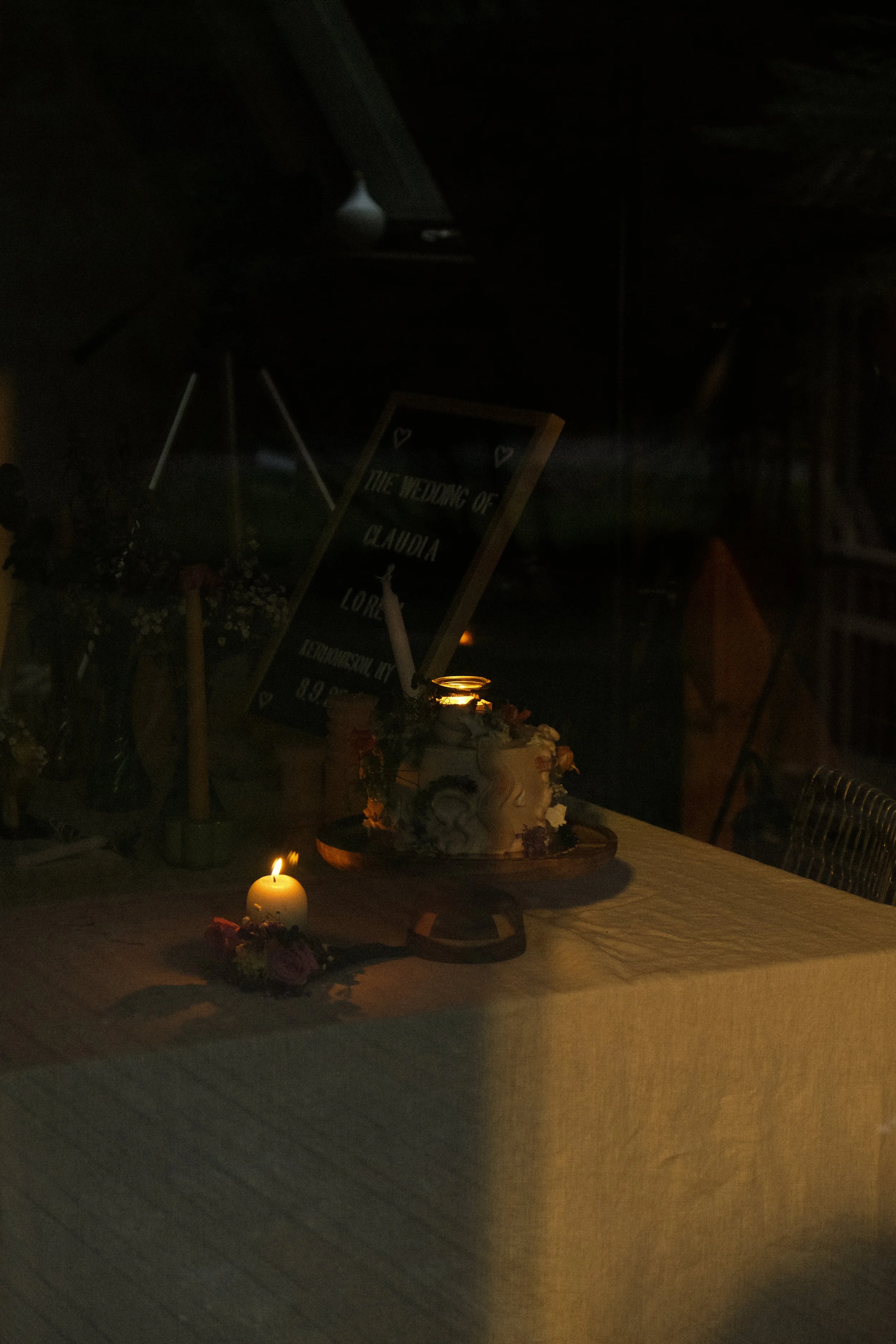 A wedding celebration display with a wedding cake on a table, lit by candles, and a sign that says "The wedding of Claudia and Lora."