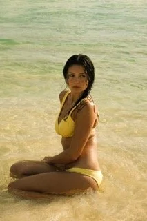 Woman in yellow swimsuit sitting in shallow water at the beach