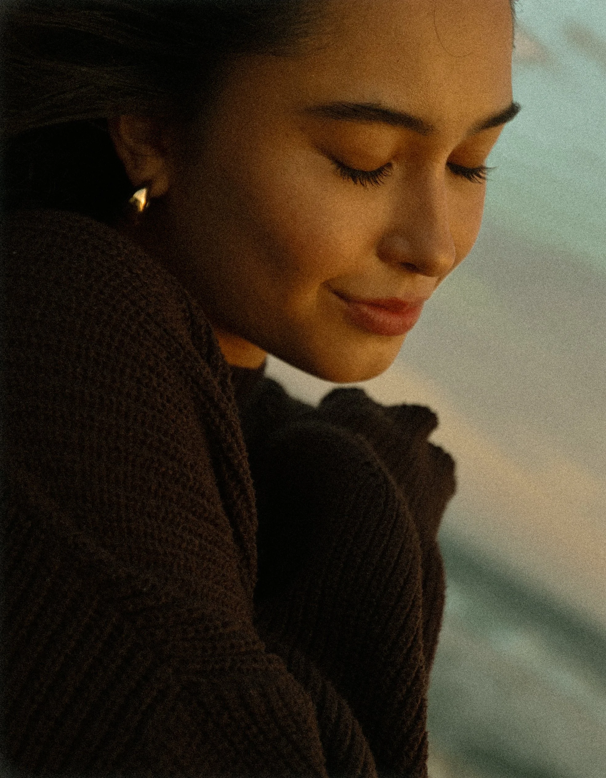Close-up of a woman with closed eyes, wearing a gold earring, with warm lighting.