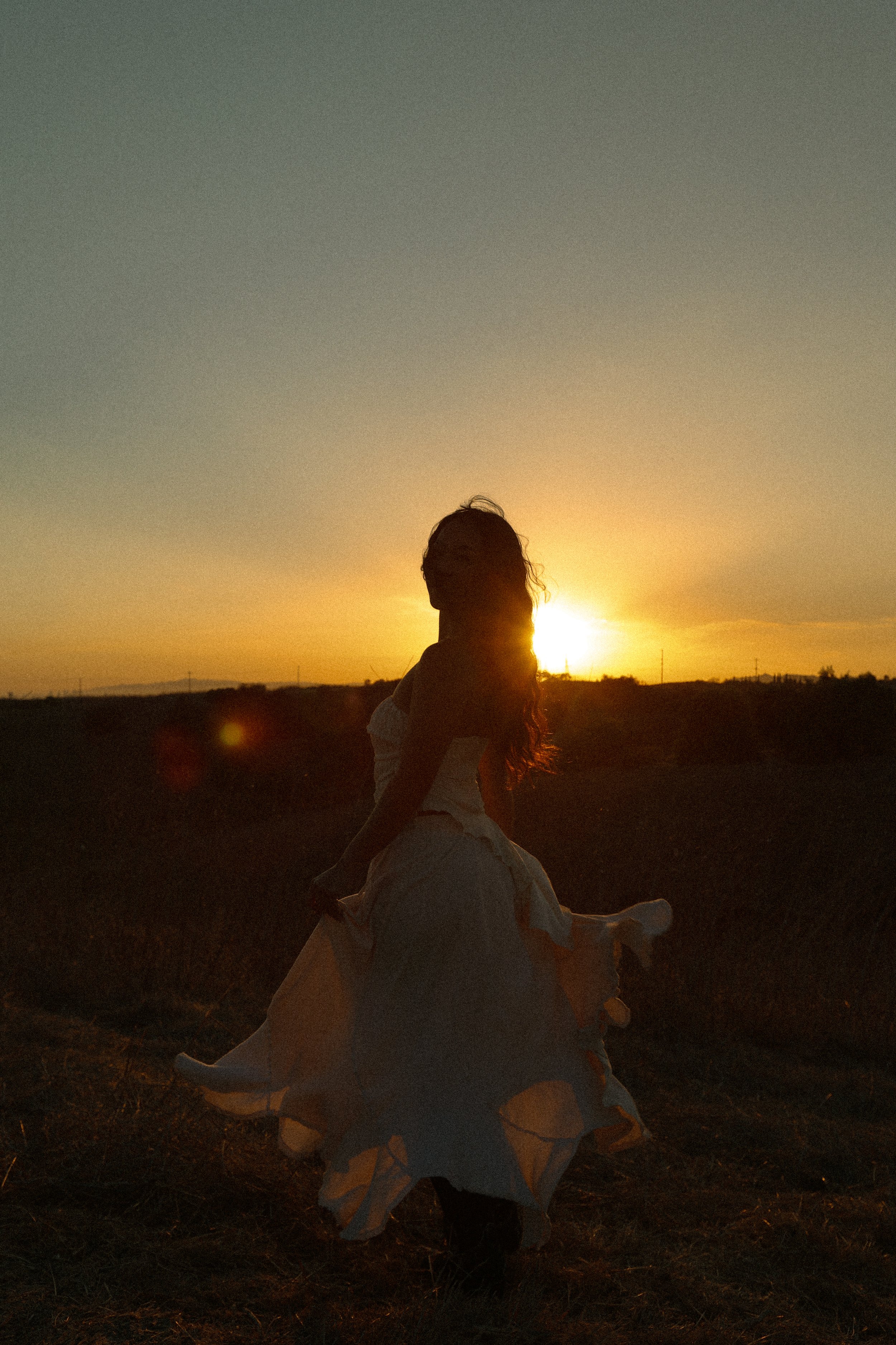 A woman in a white dress sitting on a horse during sunset in an open field.