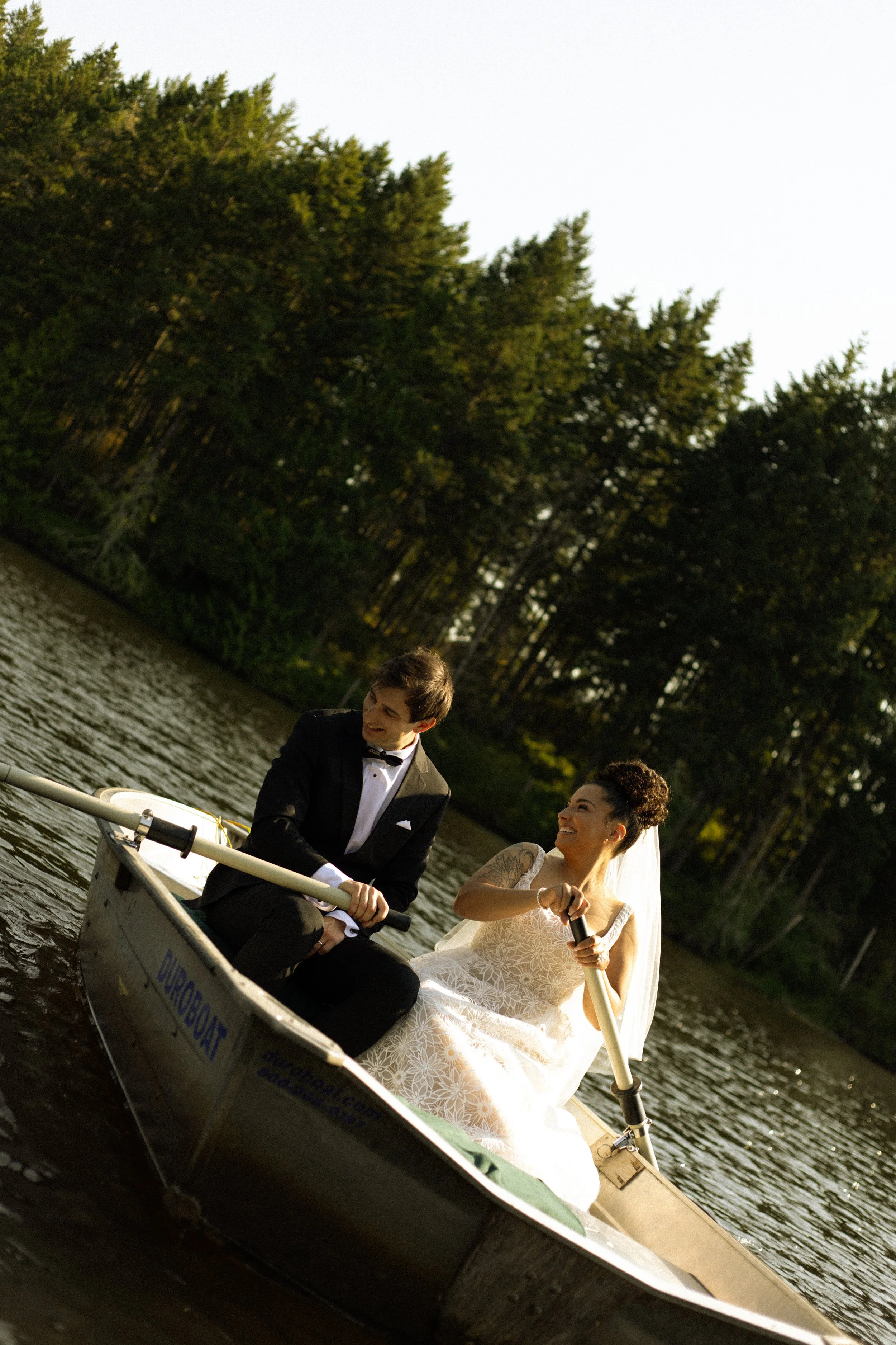 A man and woman in wedding attire rafting on a river surrounded by tall green trees.