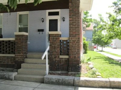 Front porch with concrete steps, brick columns, and a brick wall, attached to a blue house with white trim and a black mailbox