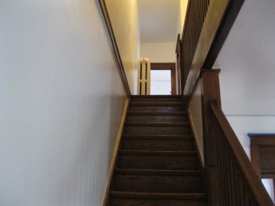 View of a wooden staircase leading up to a bright hallway with a window