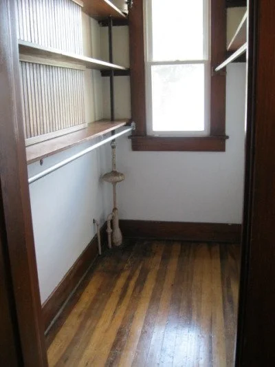 Small empty room with wooden flooring, shelves on the wall, a window, and a cat tree in the corner.