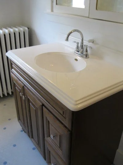 Bathroom vanity with a white sink, chrome faucet, wooden cabinet, and a mirror above.