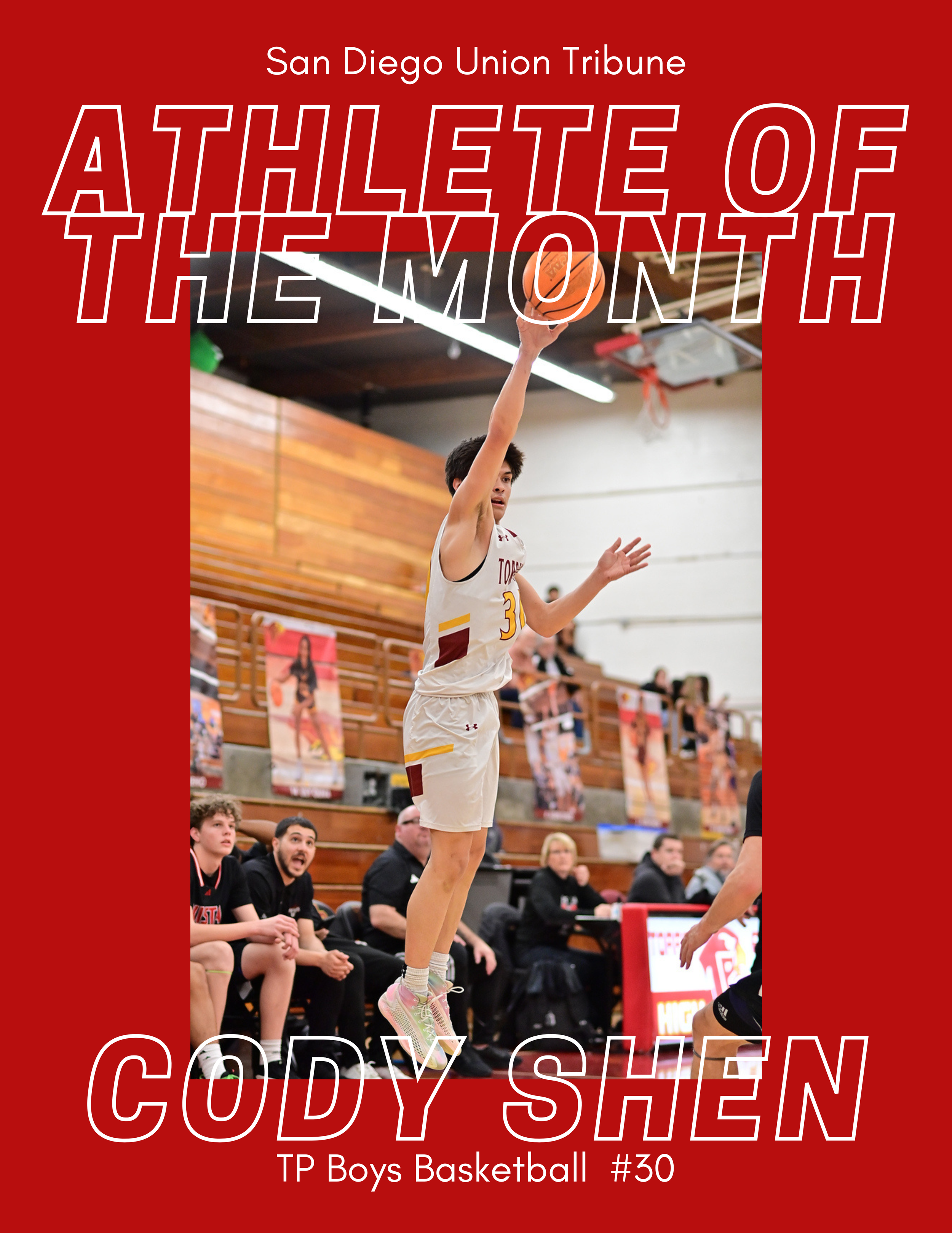 A basketball player in a white and maroon uniform jumps to shoot the ball during a game, with spectators and posters in the background.