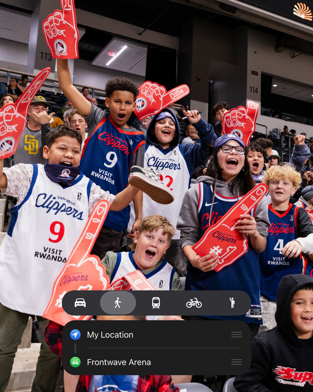 Children wearing San Diego Clippers jerseys and holding foam finger signs, cheering enthusiastically at a sports arena.
