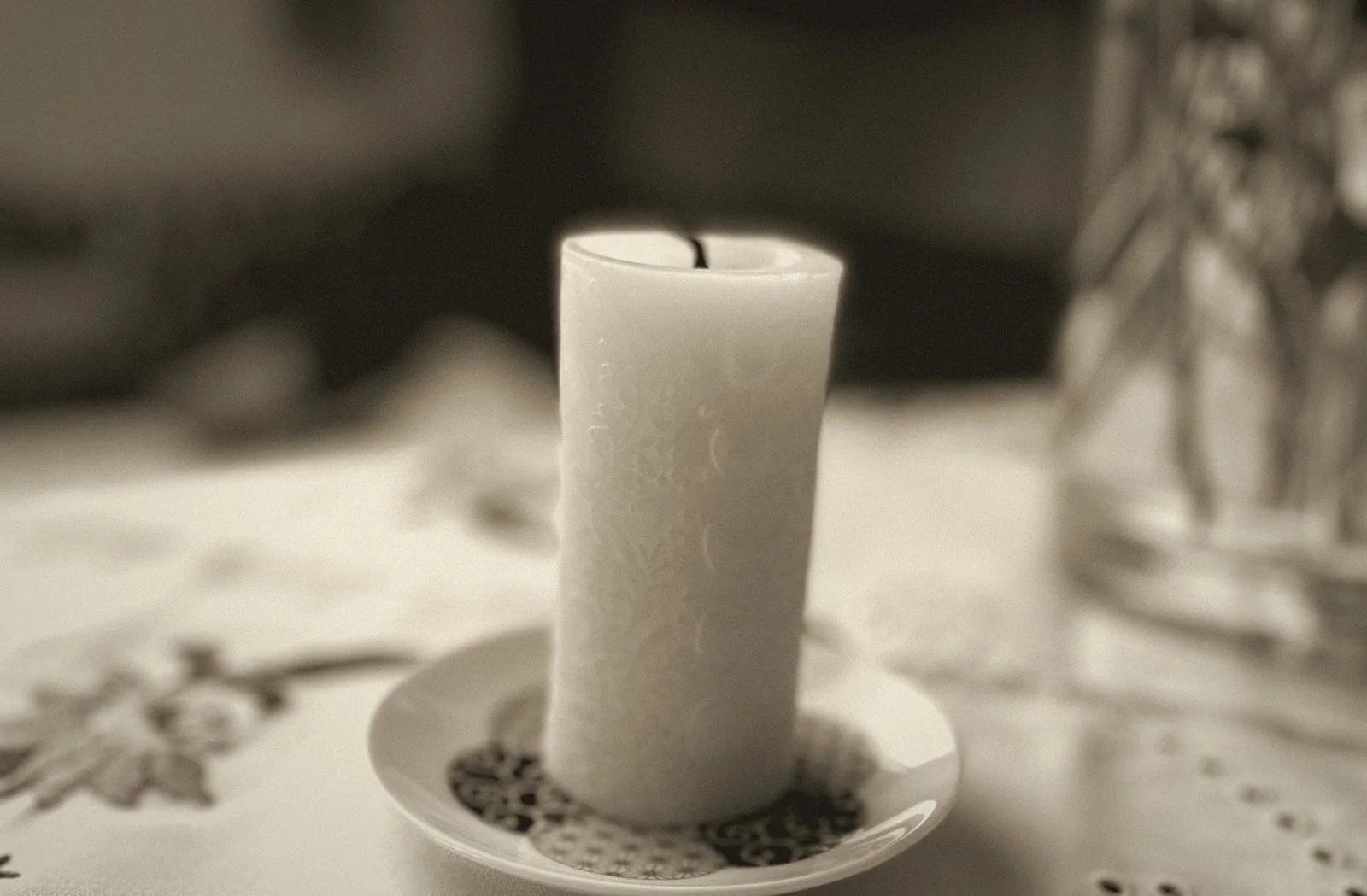 A white candle on a saucer, on an embroidered tablecloth.