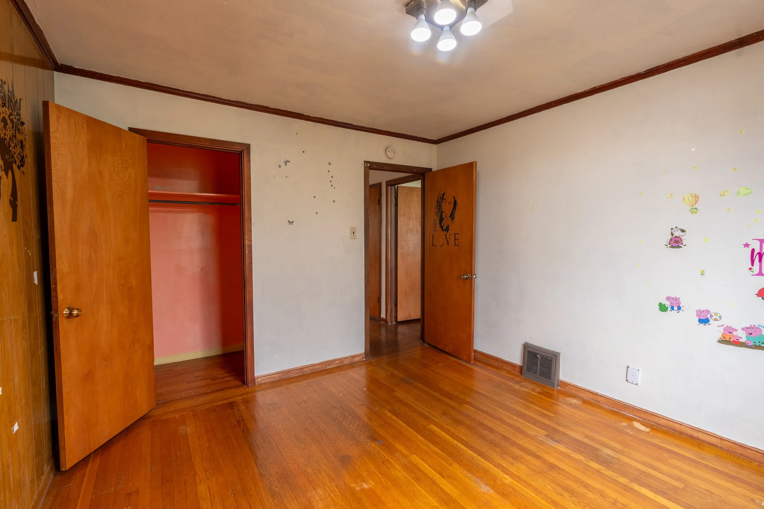 Empty room with wood floors and white walls decorated with Peppa Pig stickers. Two open wooden doors leading to different rooms.
