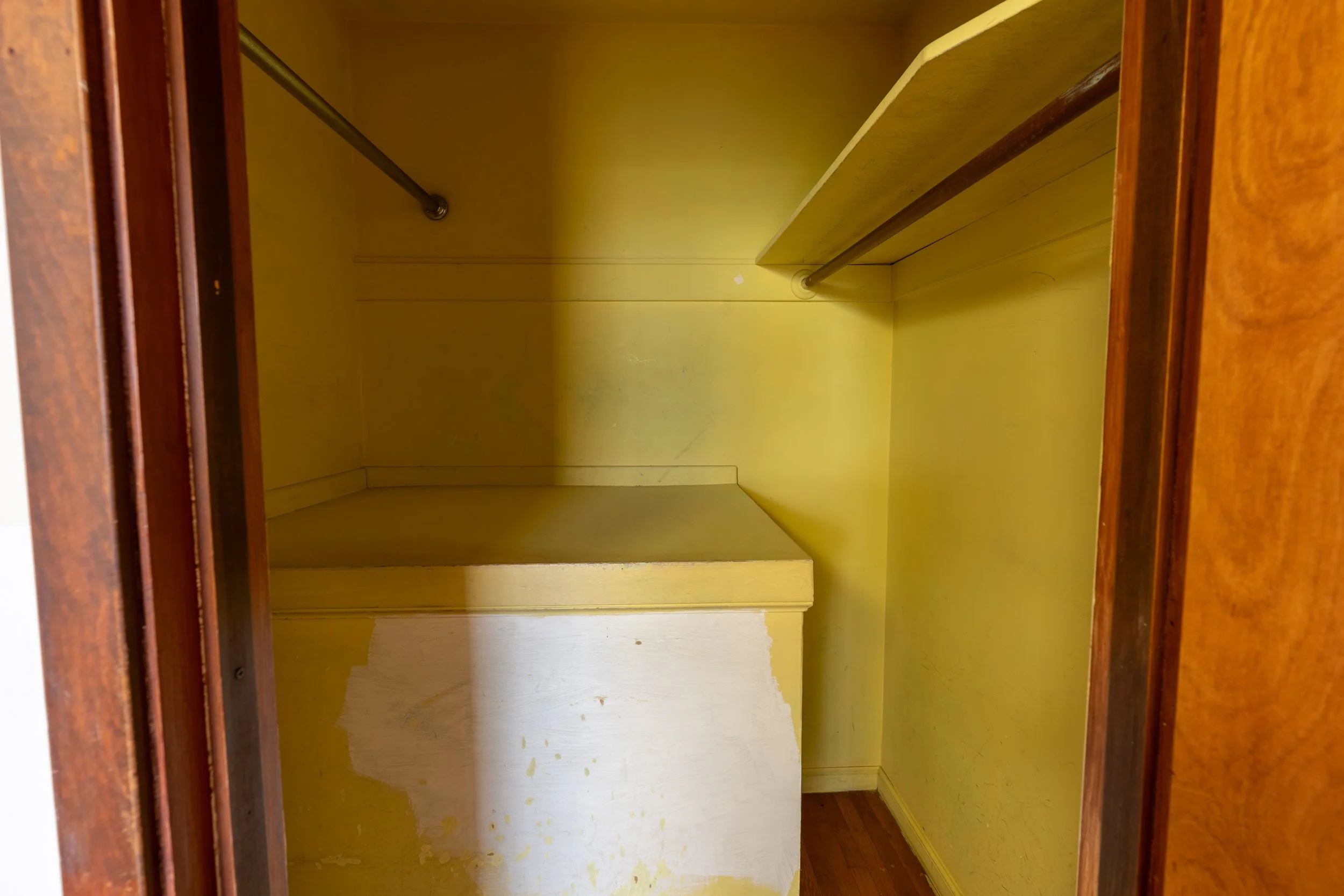 Inside an empty yellow closet with a wood frame, a metal rod for hanging clothes, and a small section of flooring visible.