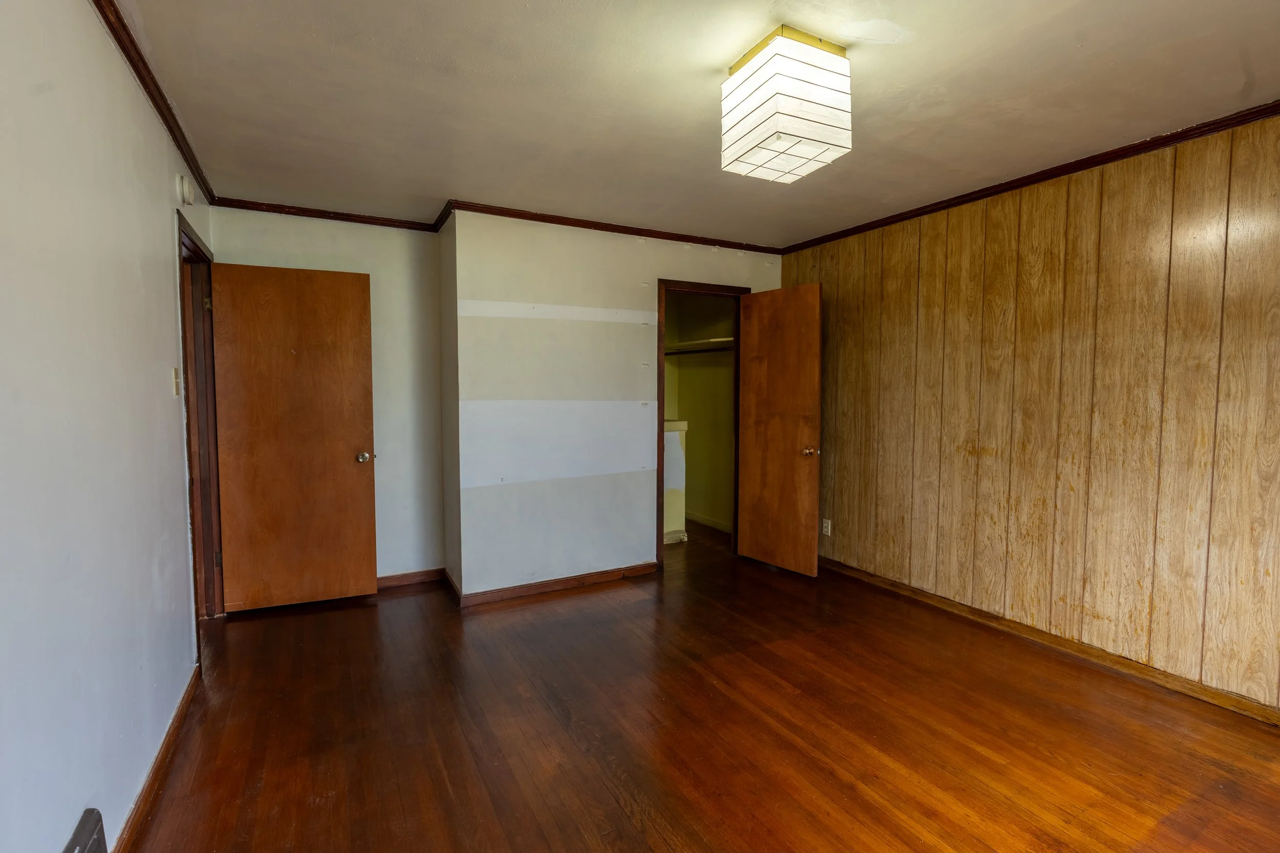 Empty room with wood floors, a closet with open doors, and wood-paneled wall.