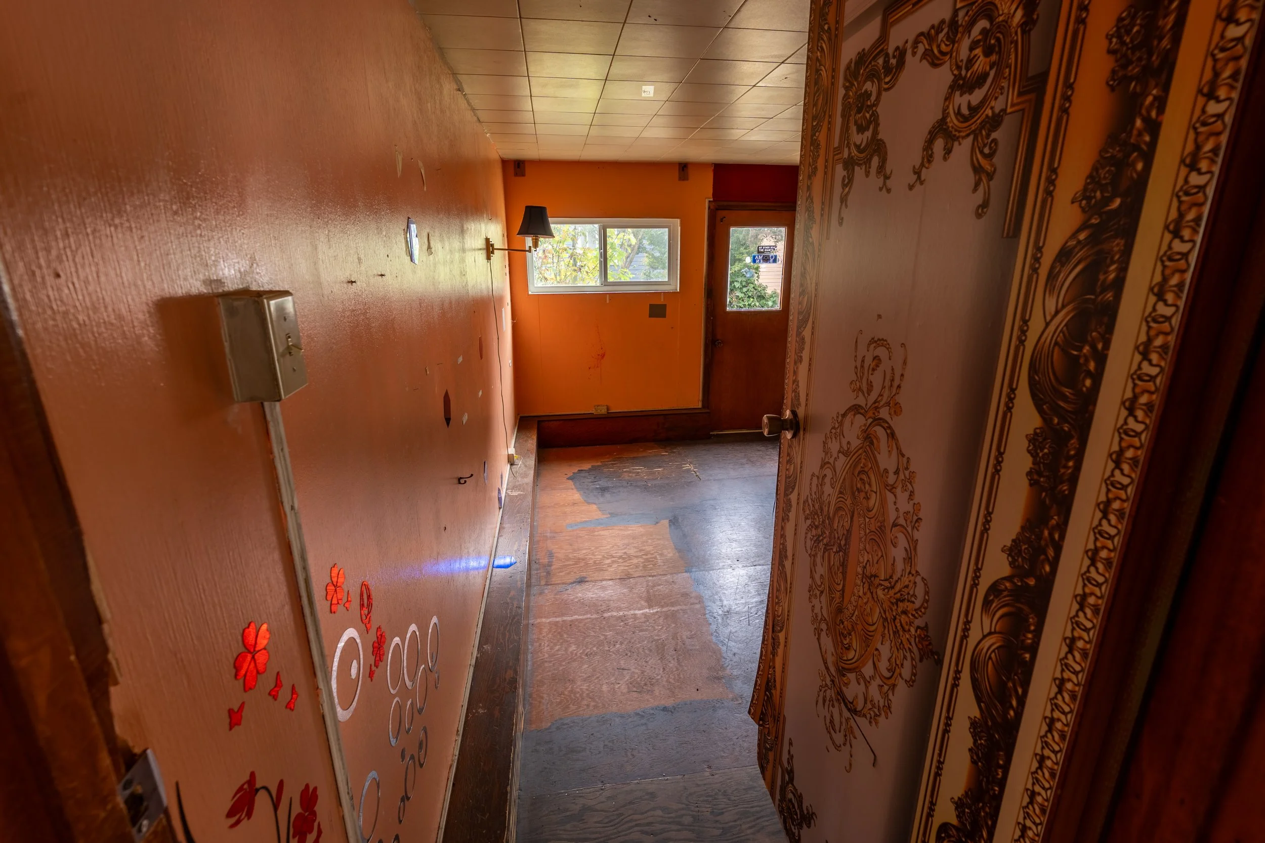 Empty room with orange walls, a window with trees outside, a black lamp on the floor, and a decorated ceiling border.