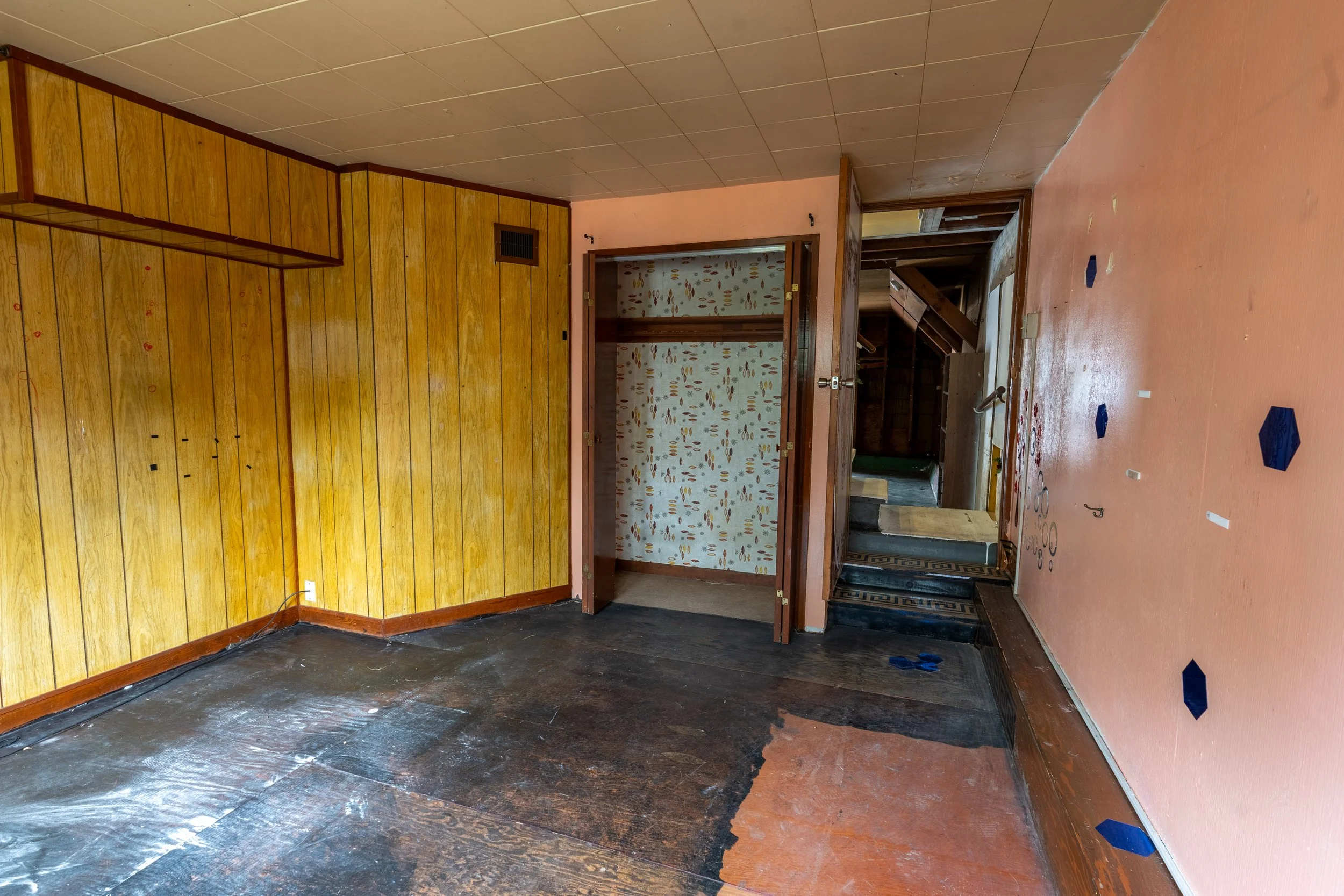 Empty room with wood-paneled walls, a doorway, and a partially painted floor with blue painter's tape.
