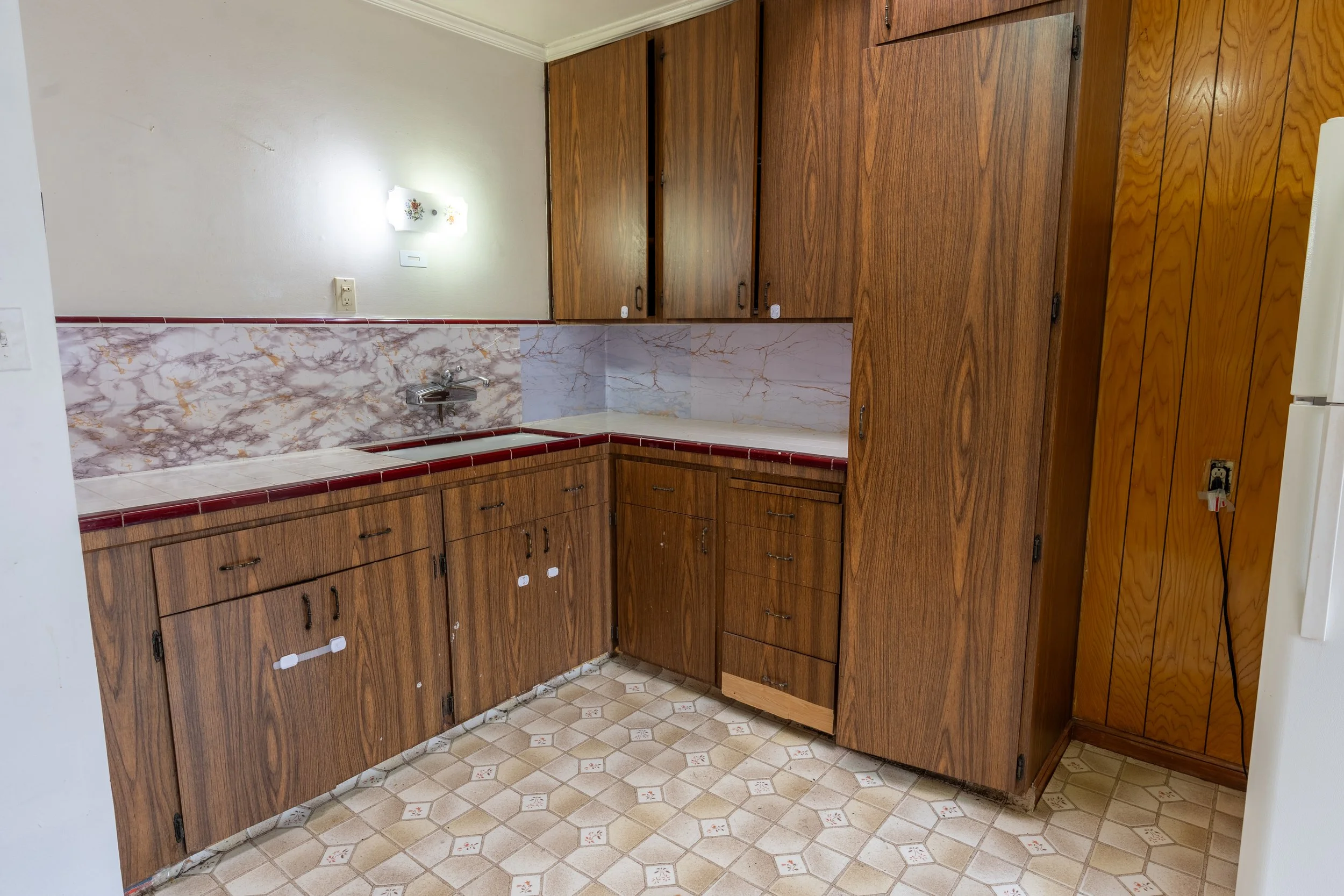 Kitchen with wooden cabinets, a marble backsplash, and tiled floor.