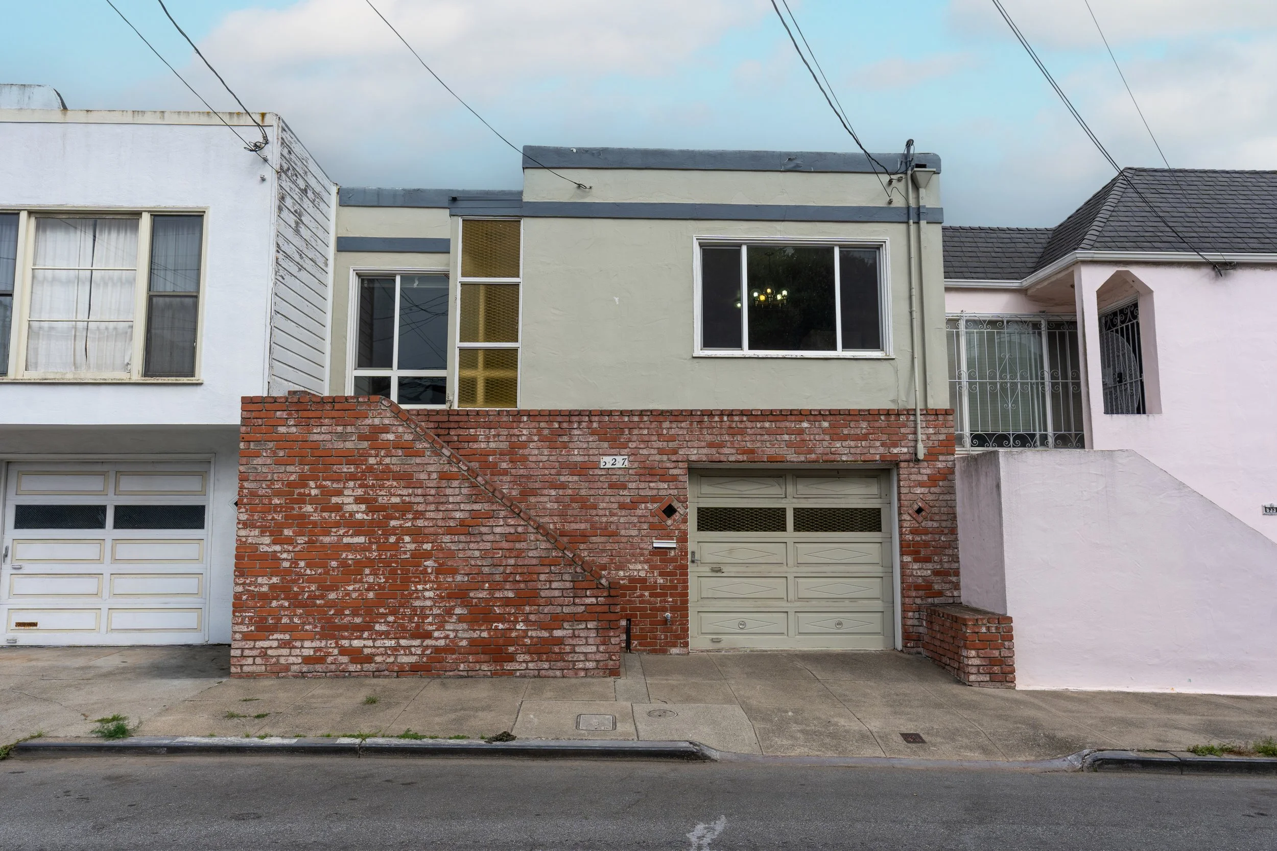 Short view of urban residential buildings with a sidewalk and street in front, featuring a mix of brick and painted walls, windows, and garage doors.
