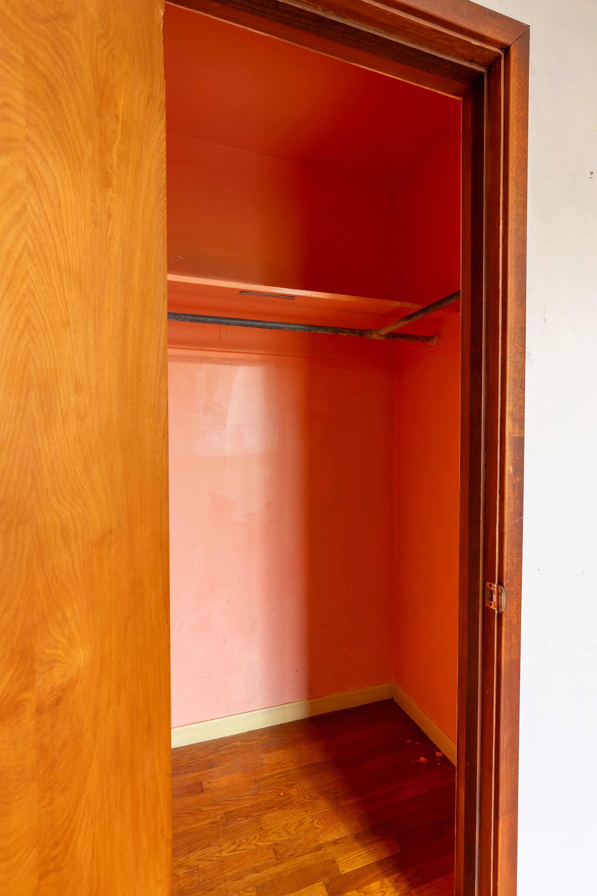 Empty closet with orange walls, wooden trim, and dark hardwood flooring, with a metal rod for hanging clothes.