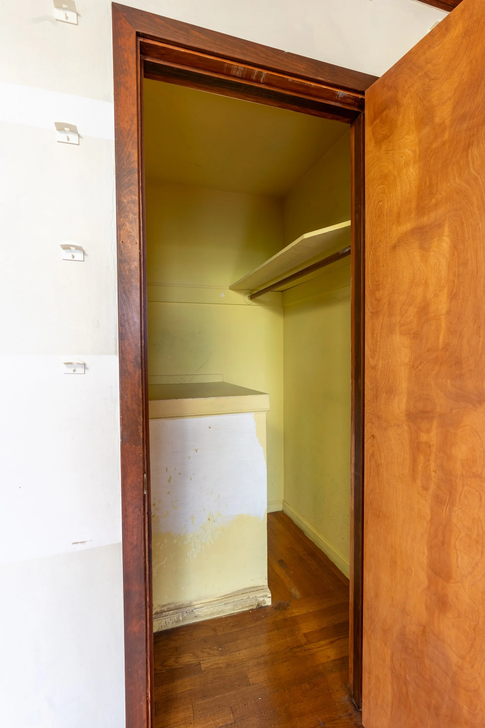 Empty closet with yellow walls, wooden floor, and a wooden shelf with a hanging rod inside.