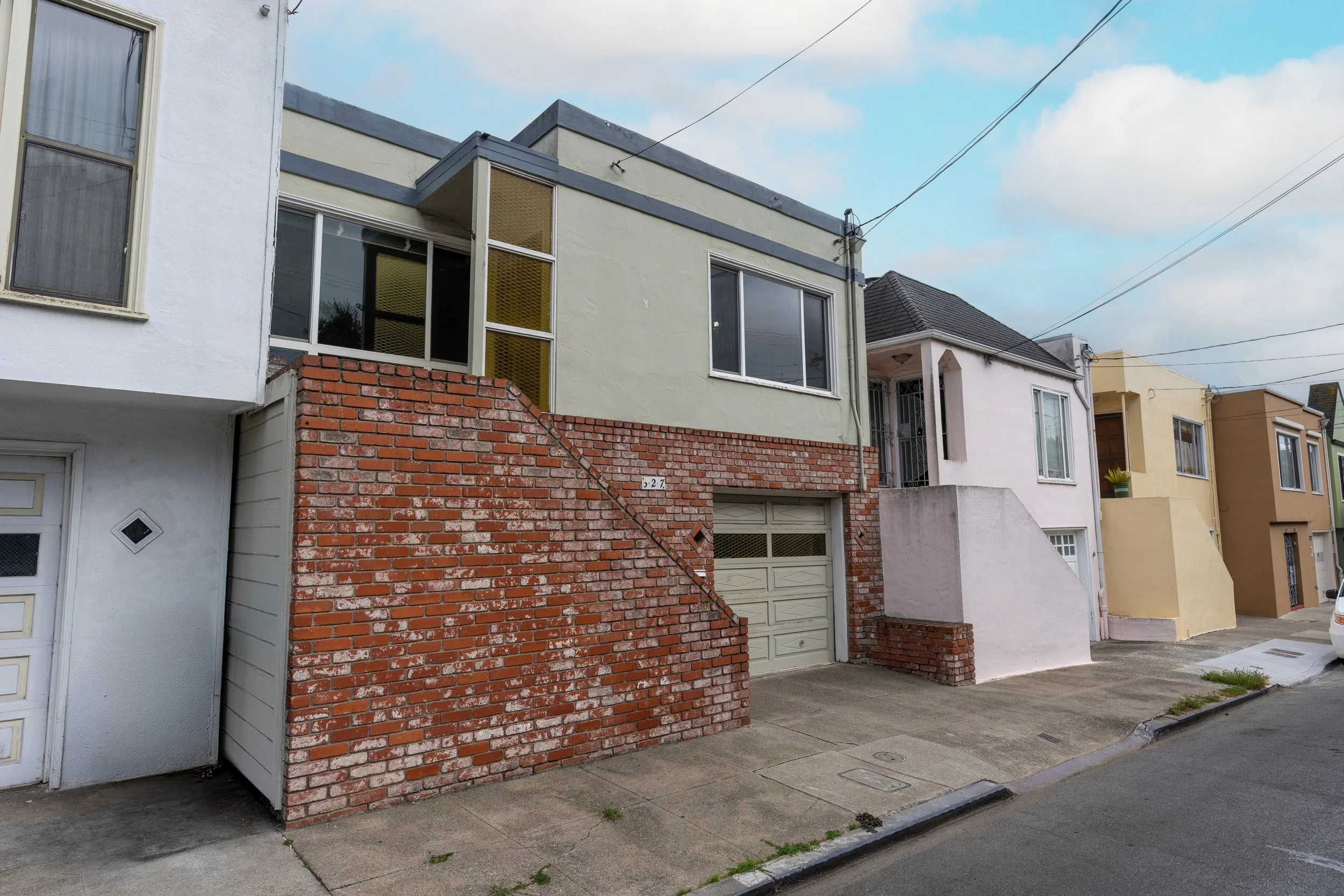 Row of houses on a street, with brick and stucco exteriors, some with garages, and overhead utility lines in the sky.