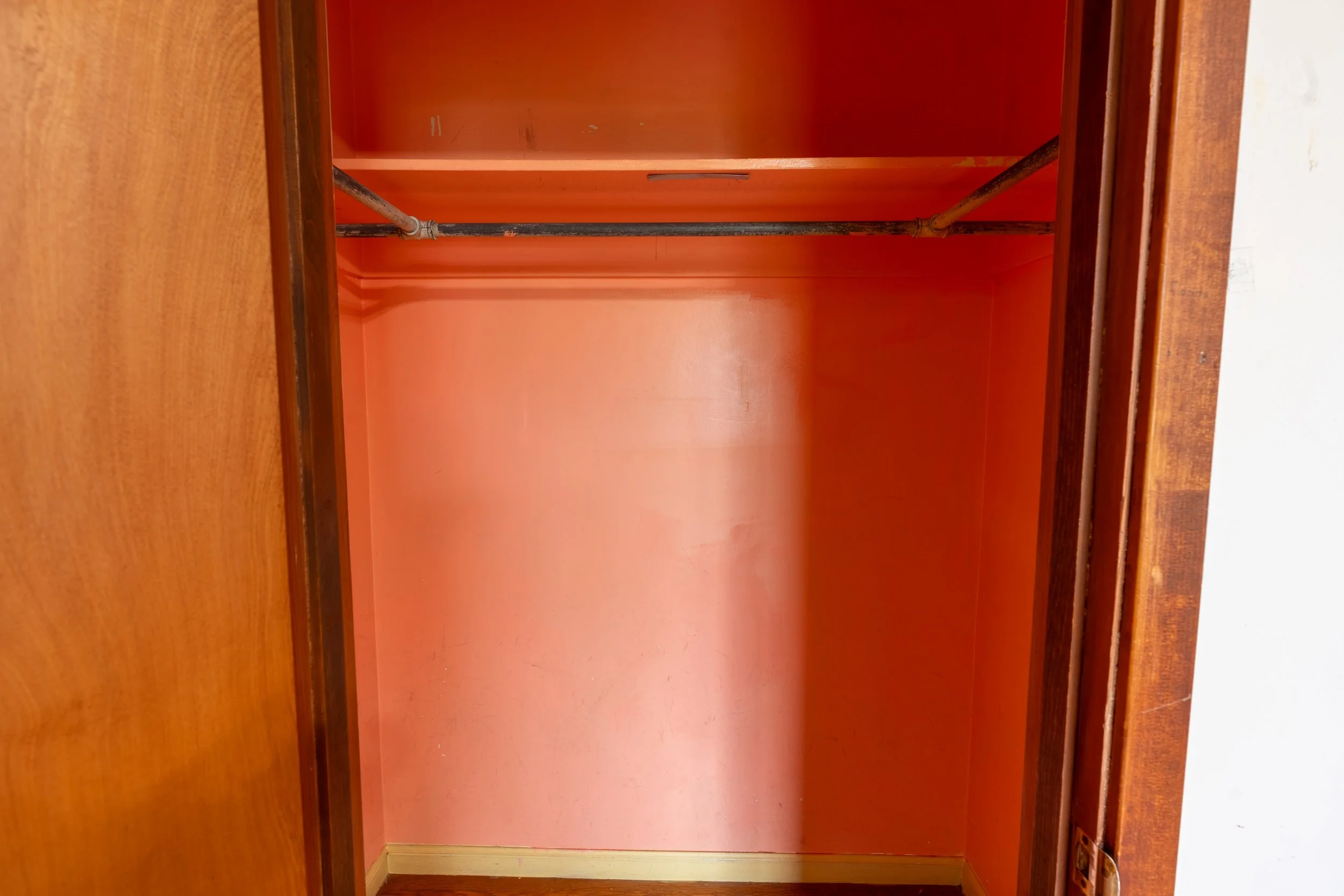 Inside of an empty wardrobe with a rod for hanging clothes, painted in pink.