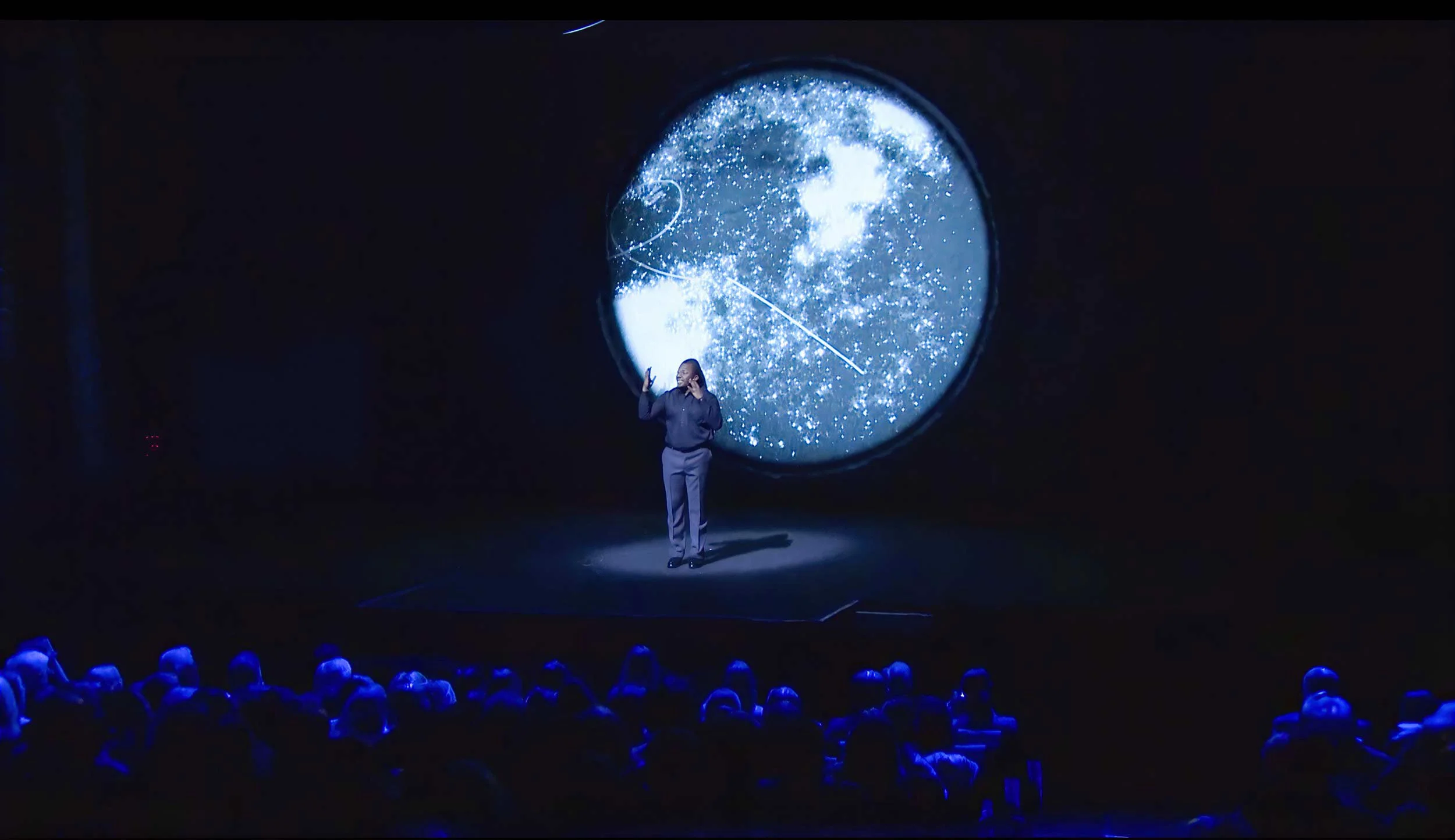 Darius reaches toward a projected painted globe glowing above the audience — The Power of Proximity, Skoll World Forum.
