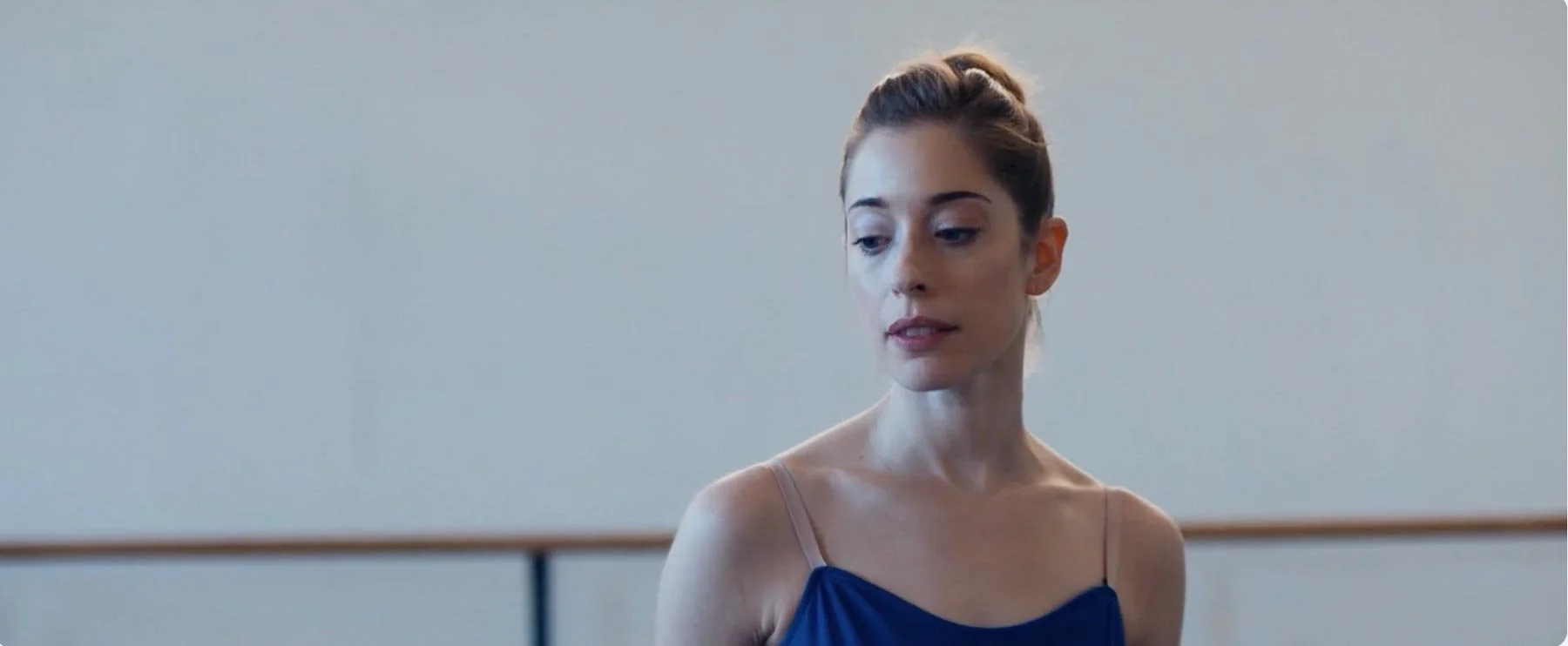 A ballerina in blue looks down thoughtfully in a rehearsal studio — The Shimmering Asphalt, New York City Ballet.