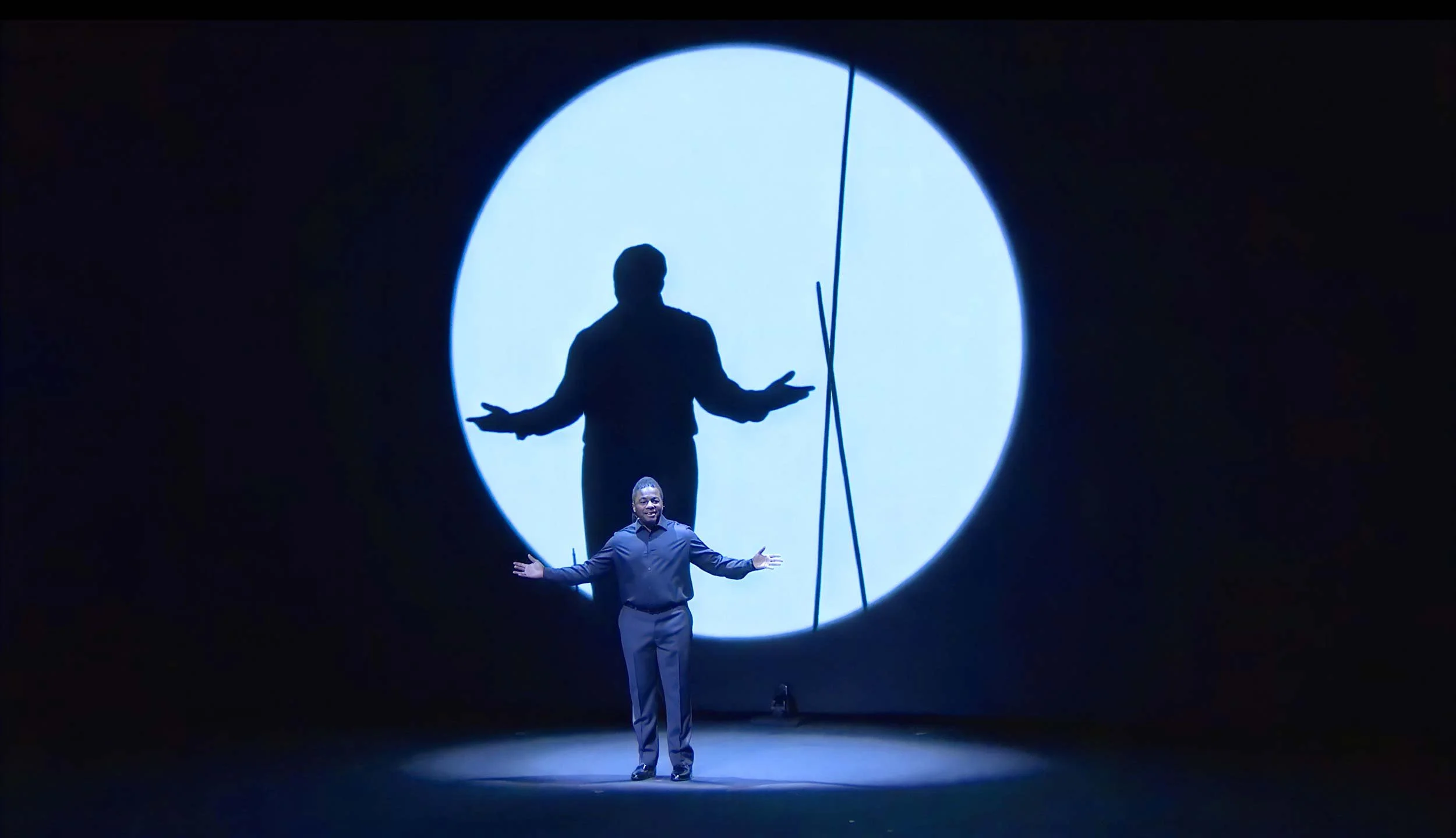 Darius spreads his arms in front of a giant projected shadow of himself in a circle of light — The Power of Proximity, Skoll World Forum.