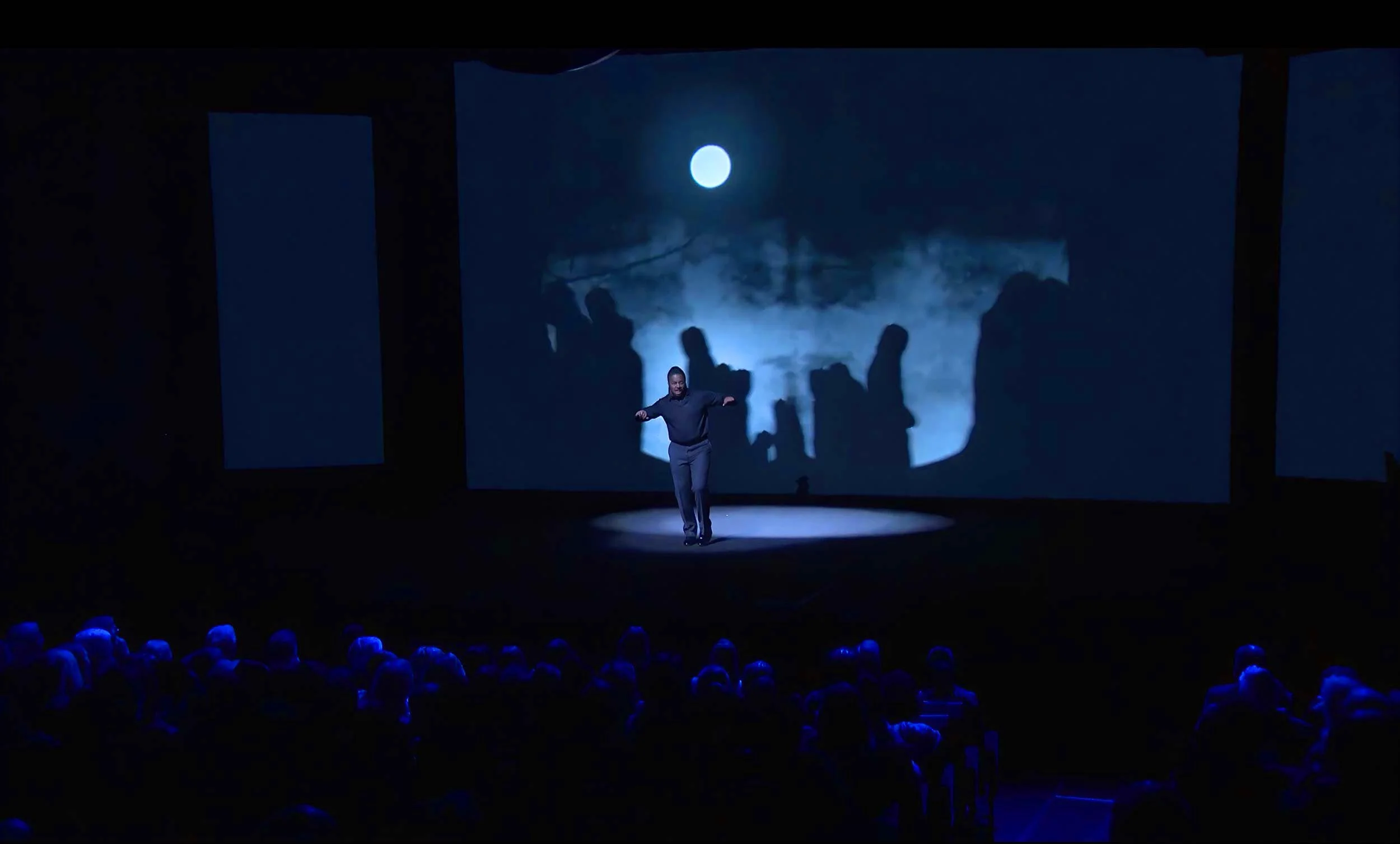 Darius stands before a projected landscape of silhouetted figures under a small moon — The Power of Proximity, Skoll World Forum.
