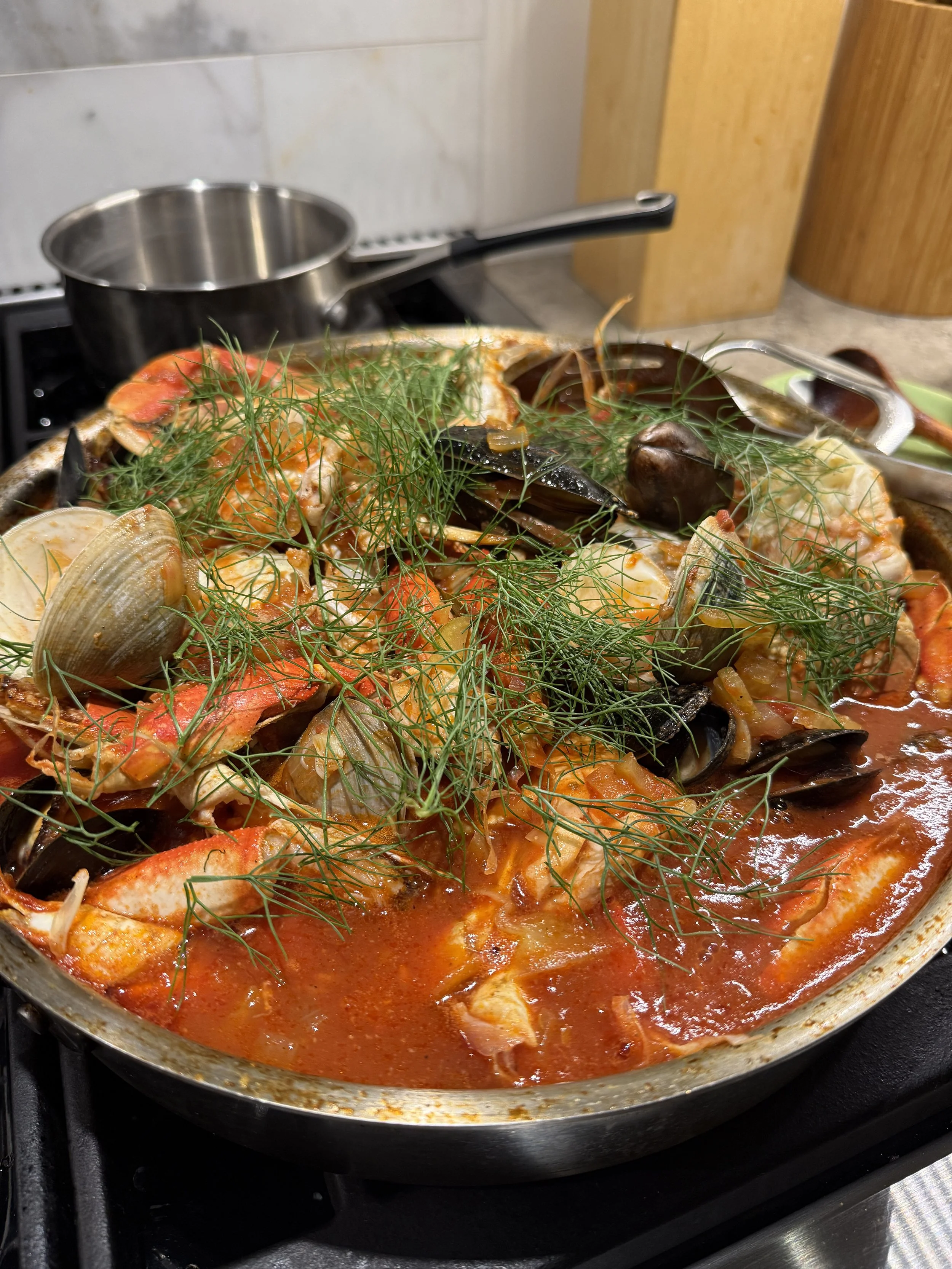 A pan on a stove with seafood, including shrimp, mussels, and clams, in a tomato-based sauce, garnished with fresh herbs.