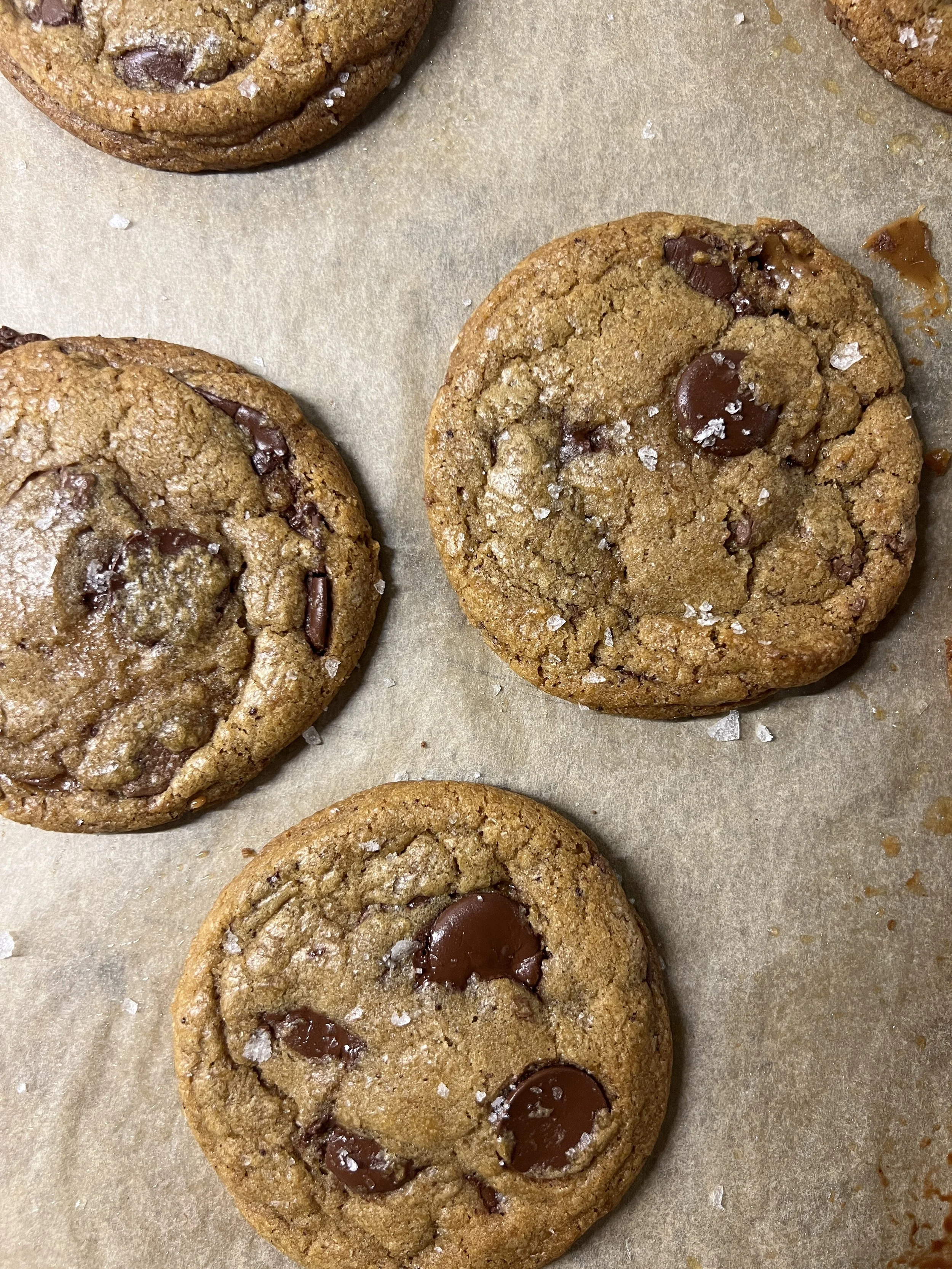 Close-up of freshly baked chocolate chip cookies with salt flakes on top, on a parchment paper-lined baking sheet.