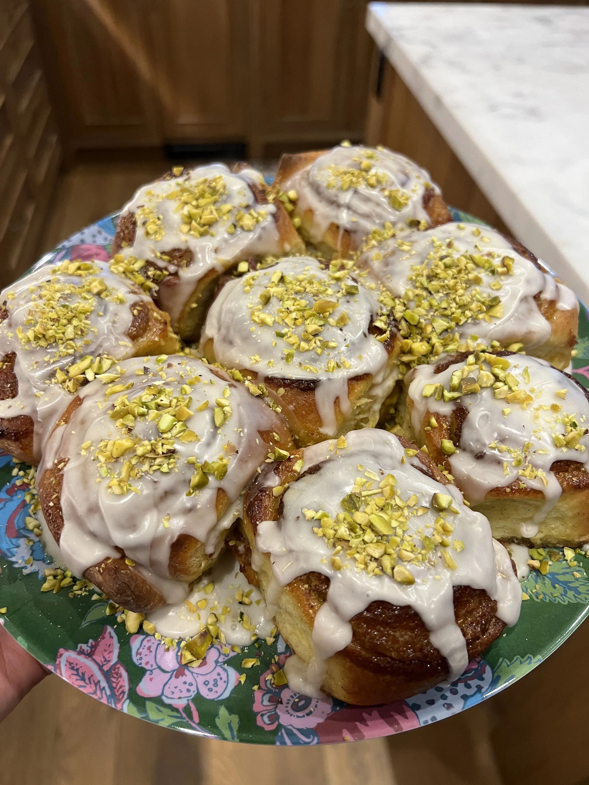 Close-up of a plate of cinnamon rolls topped with white icing and chopped pistachios.