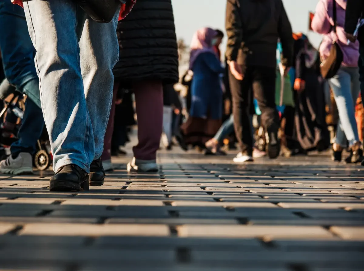 Close-up of the legs and feet of many different people walking on a roadway made of small square pavers. Elliott Haverlack's message is for everyone.