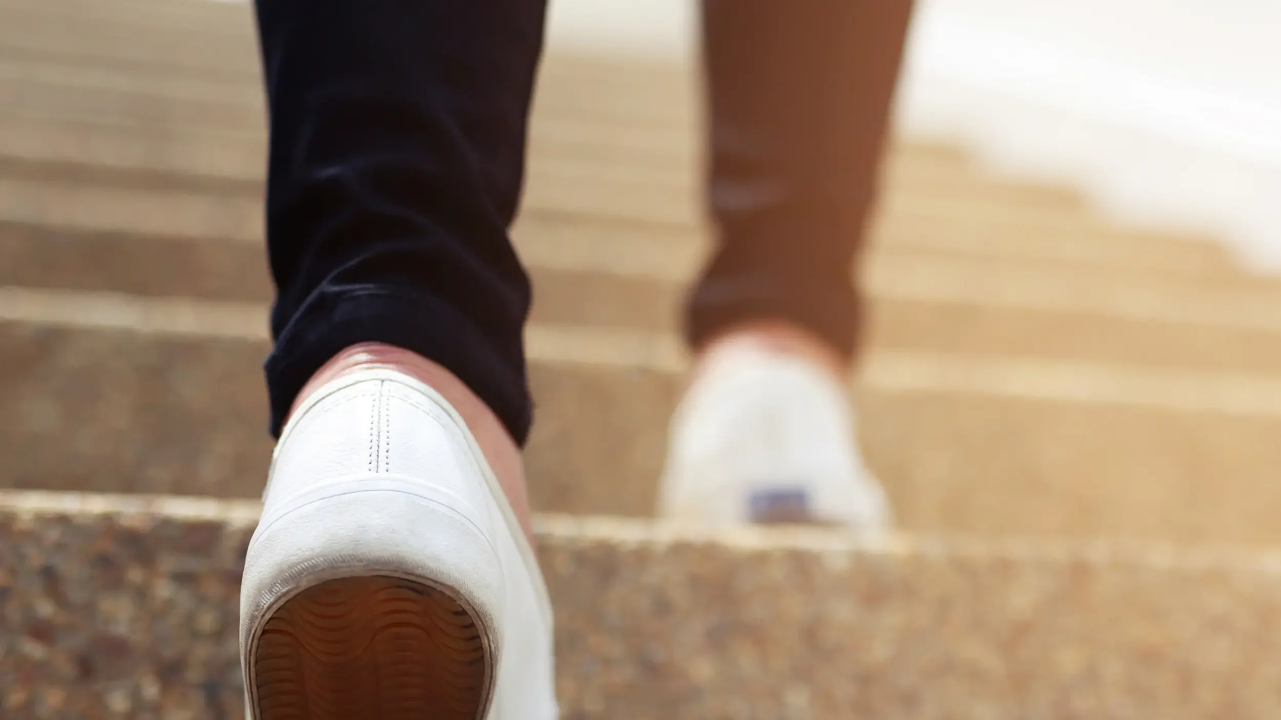 close-up of feet wearing white flat tennis shoes walking up a set of cement steps