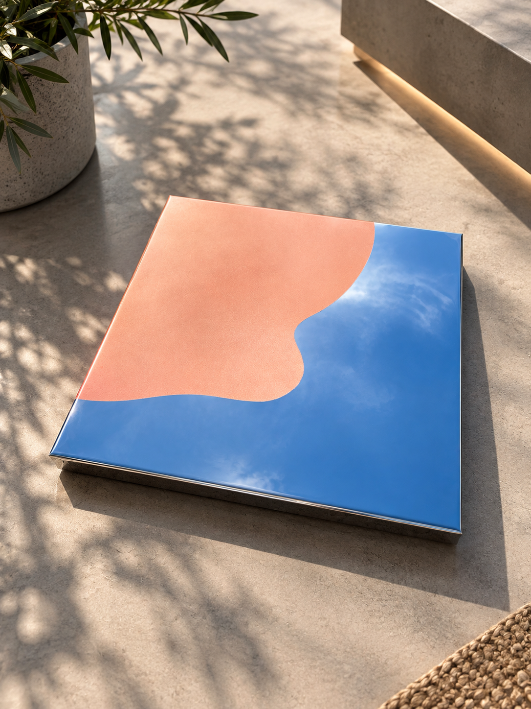 Modernes Spiegel-Artwork mit reflektierendem Himmel und Wolken, auf glattem Boden, neben einer Pflanze