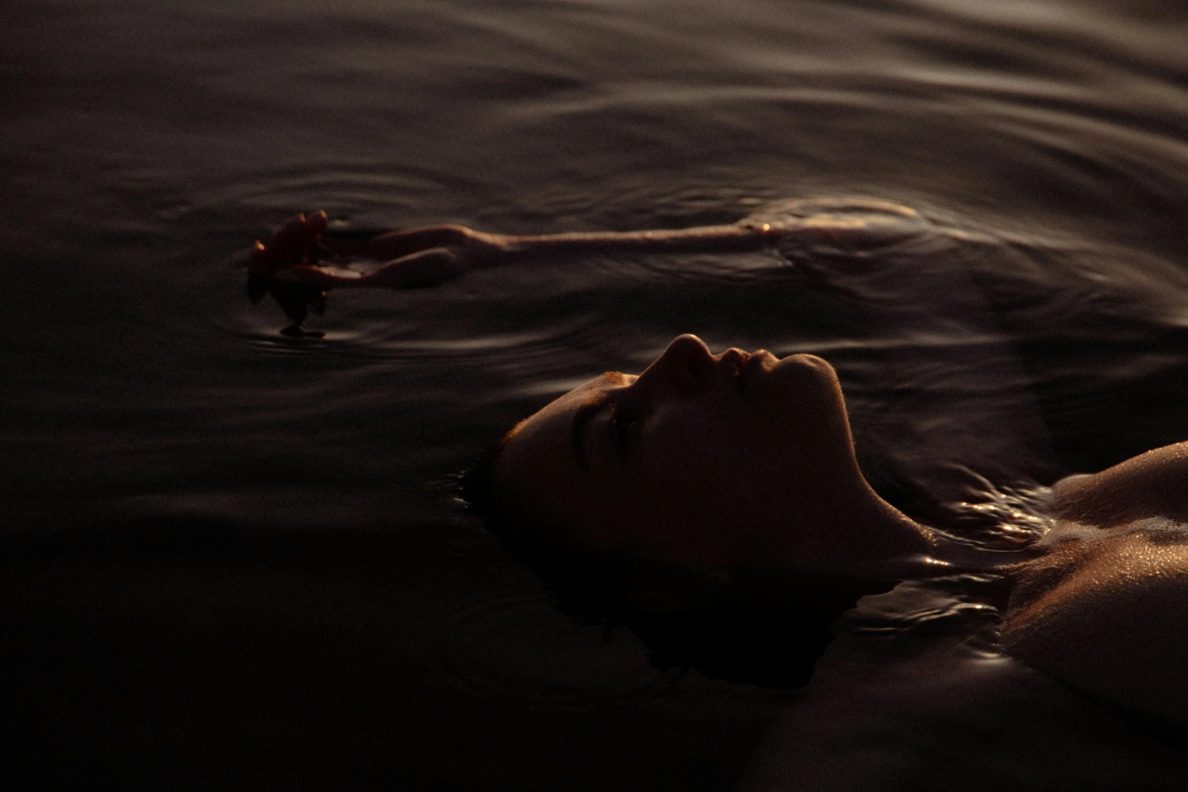 Eine Person liegt entspannt im Wasser und schaut nach oben, während das Wasser im warmen Licht des Sonnenuntergangs glitzert.