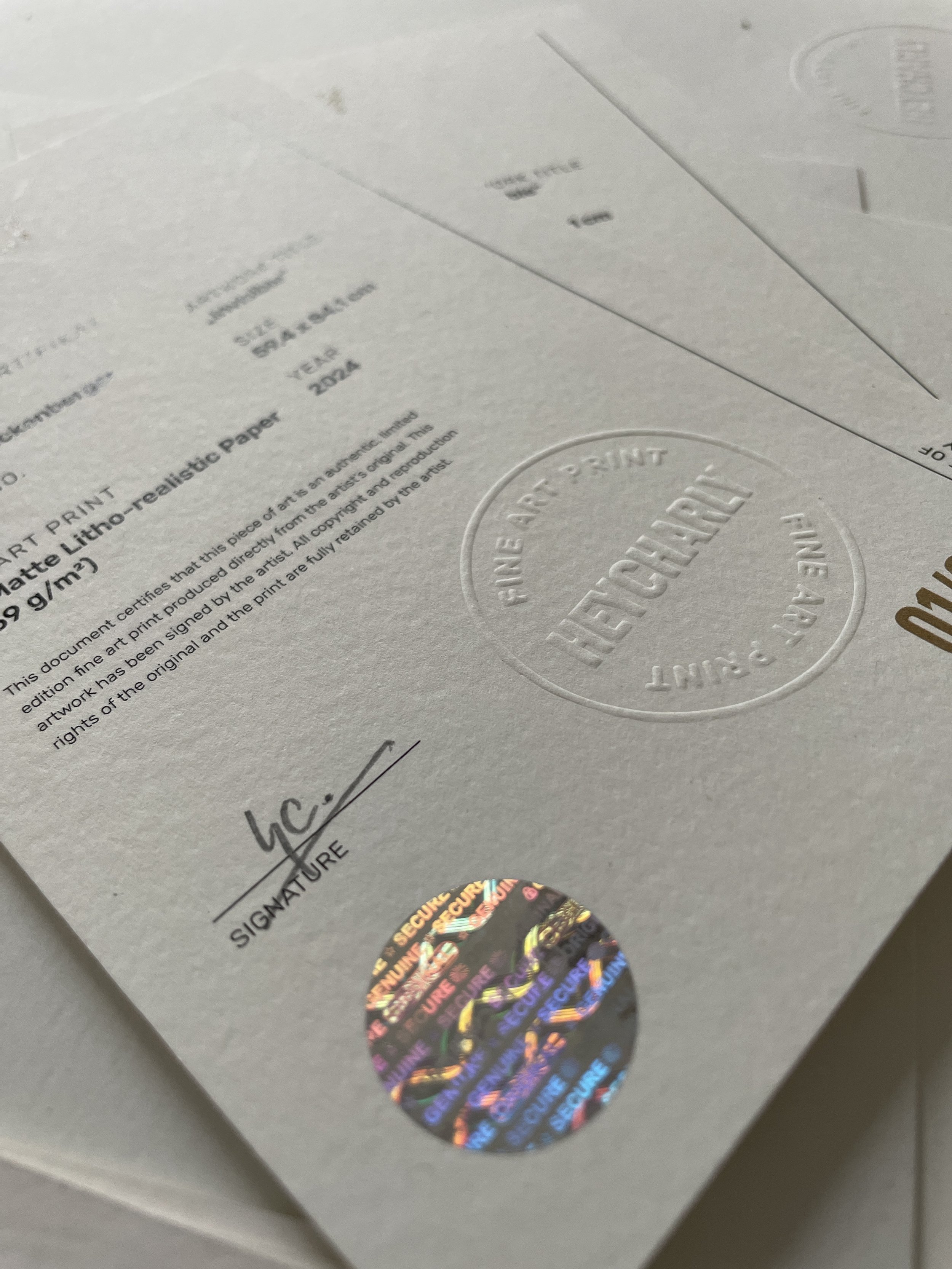 Ein weißes Zertifikat mit dem Text 'CERTIFICATE OF AUTHENTICITY' und einem holographischen Sicherheitssticker darunter.