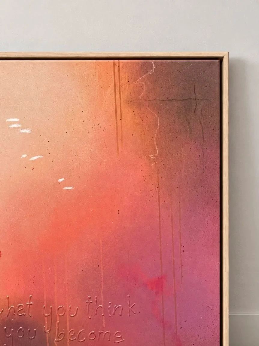 Ein Wandbild mit warmen Farbtönen in Pink, Orange und Braun, das einige Details und Sprenkel zeigt. Im unteren Bereich sind im Licht sanft erhabene Worte zu lesen, die sagen: 'what you think you become'.