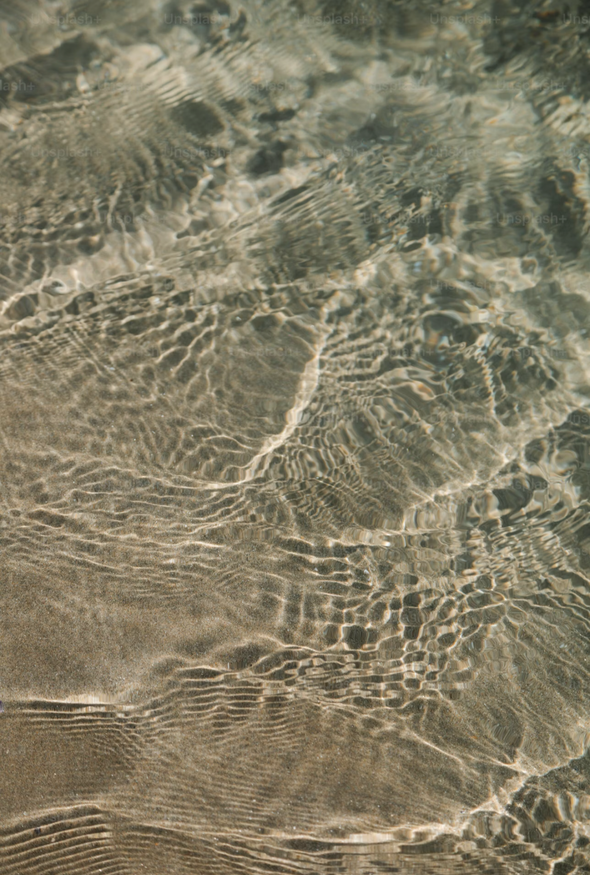 Nahaufnahme von Wasser auf Sandstrand, Wasseroberfläche mit Lichtreflexen und Wellenmustern.