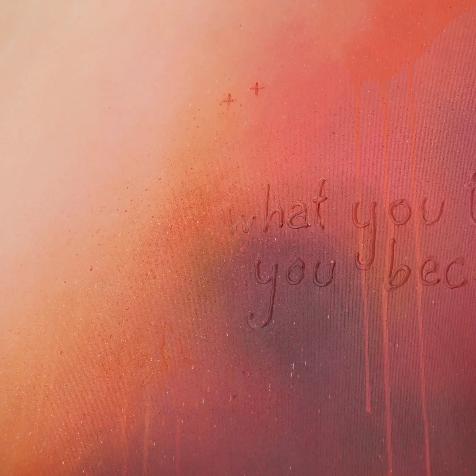 Ein Wandbild mit warmen Farbtönen in Pink, Orange und Braun, das einige Details und Sprenkel zeigt. Im unteren Bereich sind im Licht sanft erhabene Worte zu lesen, die sagen: 'what you think you become'.