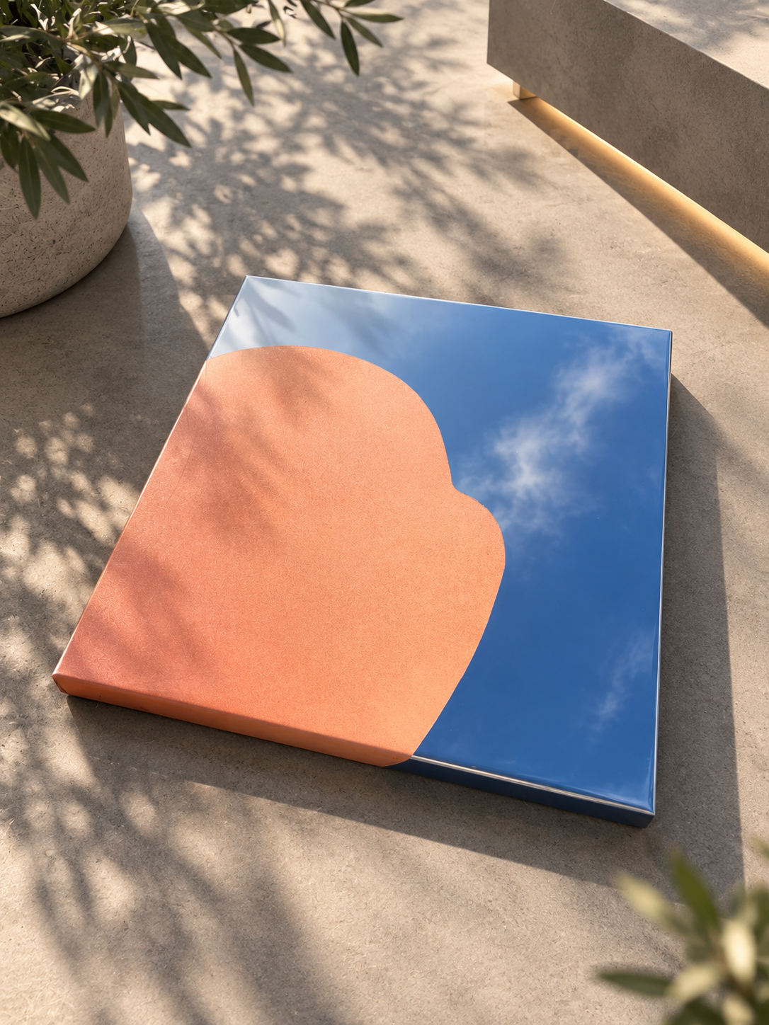 Modernes Spiegel-Artwork mit reflektierendem Himmel und Wolken, auf glattem Boden, neben einer Pflanze