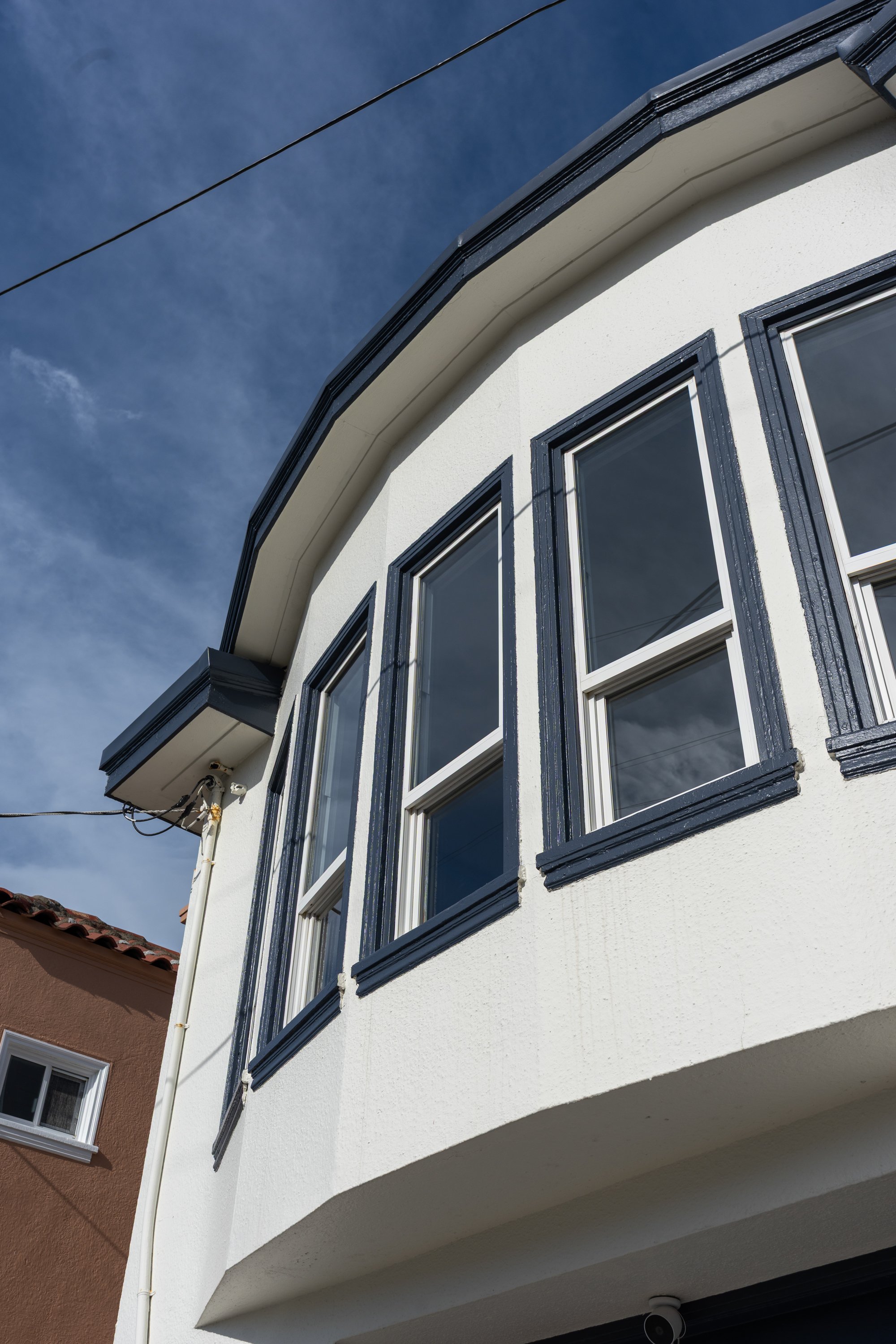 Close-up of the upper part of a white building with three windows and black trim, under a blue sky with some clouds