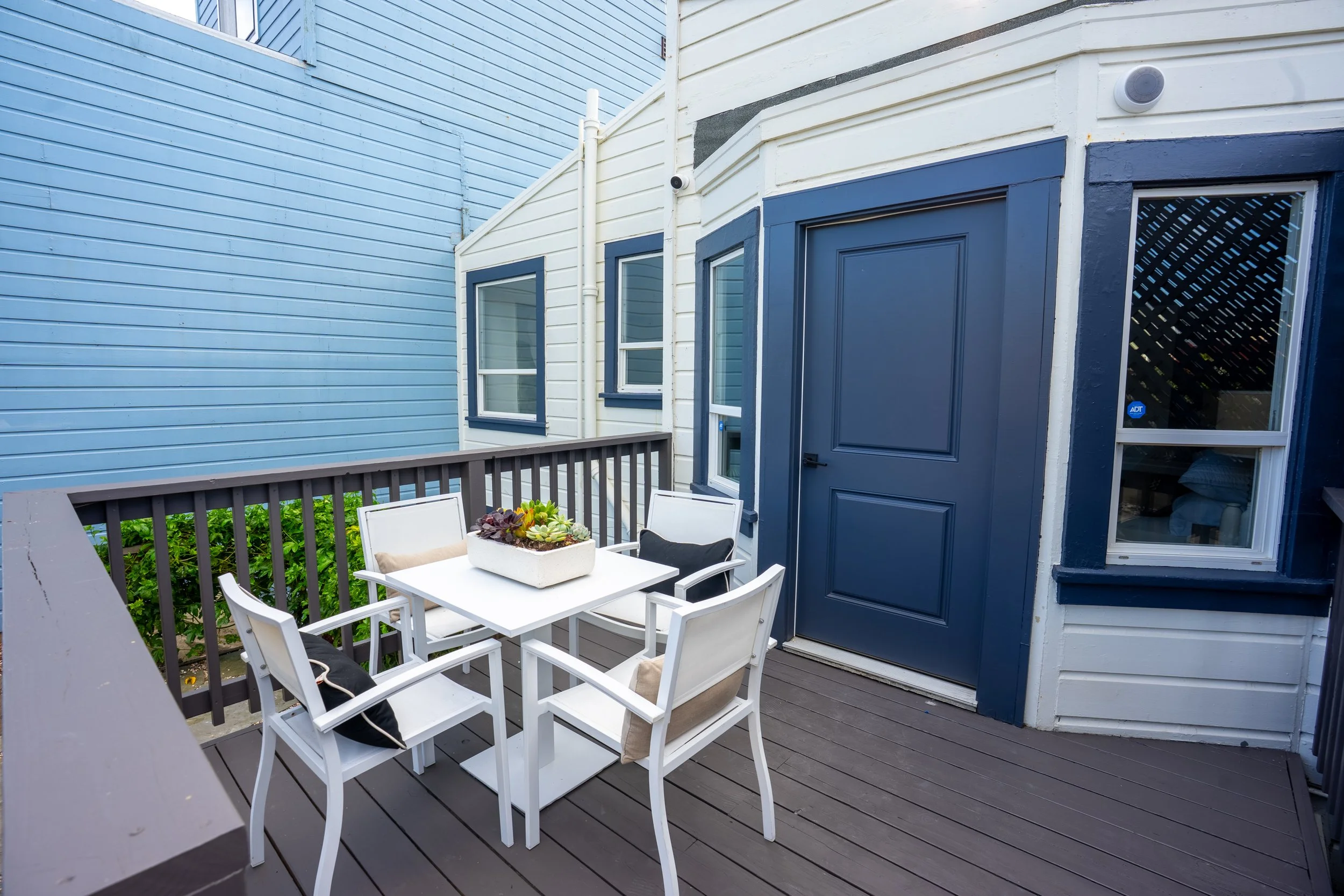 Small outdoor patio with white chairs and a table, featuring a centerpiece with succulents, enclosed by blue and white painted wooden walls.