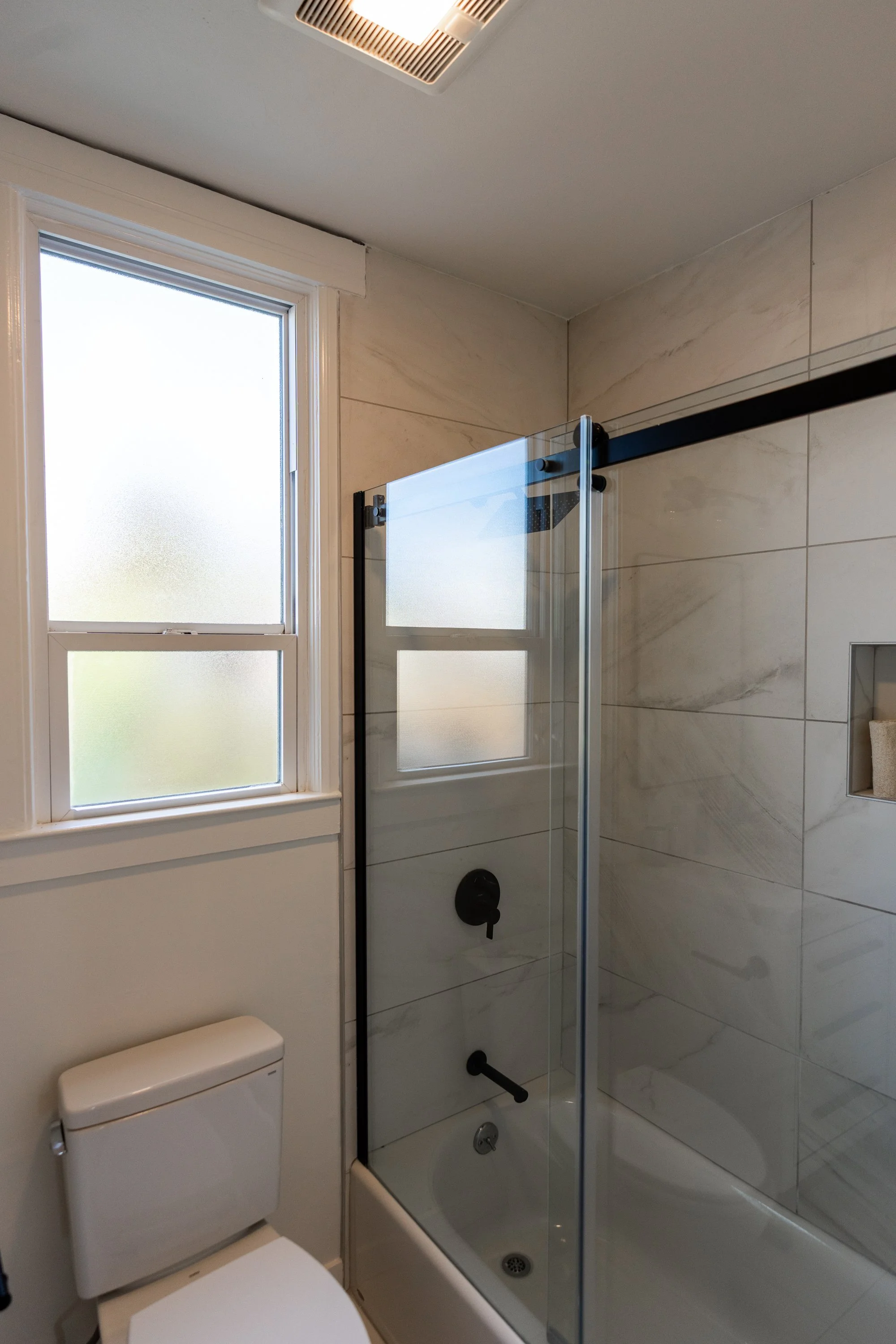 Bathroom with frosted window, tiled walls, glass shower enclosure, and a toilet.