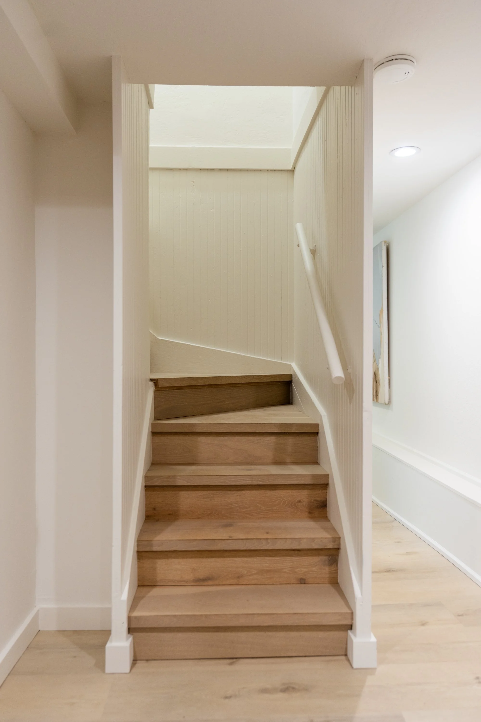 Wooden staircase with white railing leading up to a small landing and an open skylight in the ceiling.
